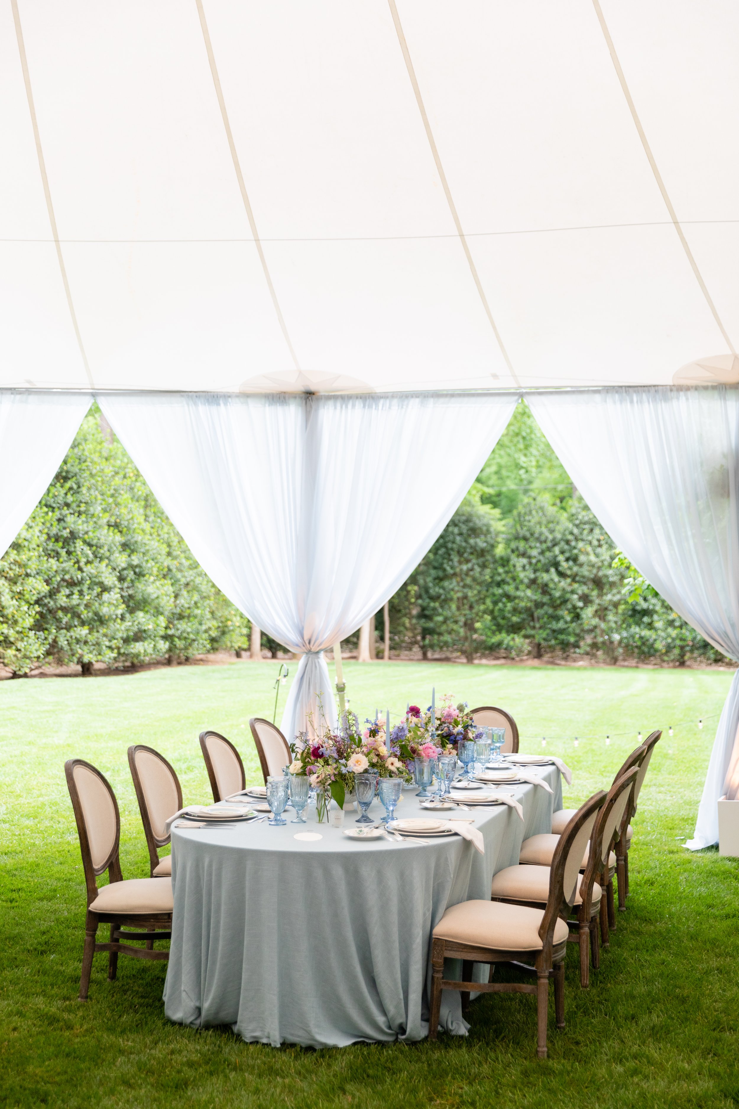 Growing, fresh floral centerpieces with blush garden roses, lilac, blue sweet peas, ranunculus, lavender delphinium, globe allium, clematis, and natural greenery for a tented Bridgerton inspired engagement party at a private home in Nashville, TN.