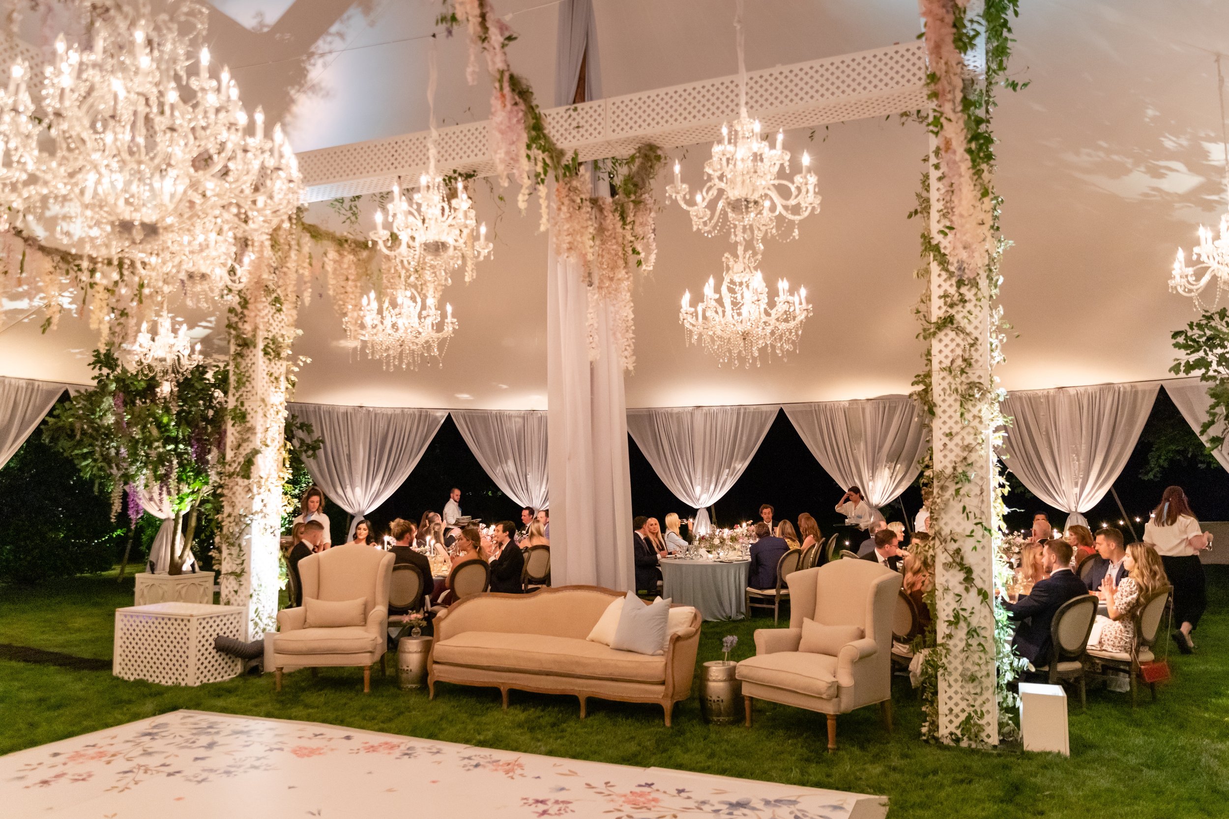 Growing, fresh floral installations and chandeliers with blush garden roses, lavender delphinium, wisteria, globe allium, and vines and greenery for a tented Bridgerton inspired engagement party at a private home in Nashville, TN.