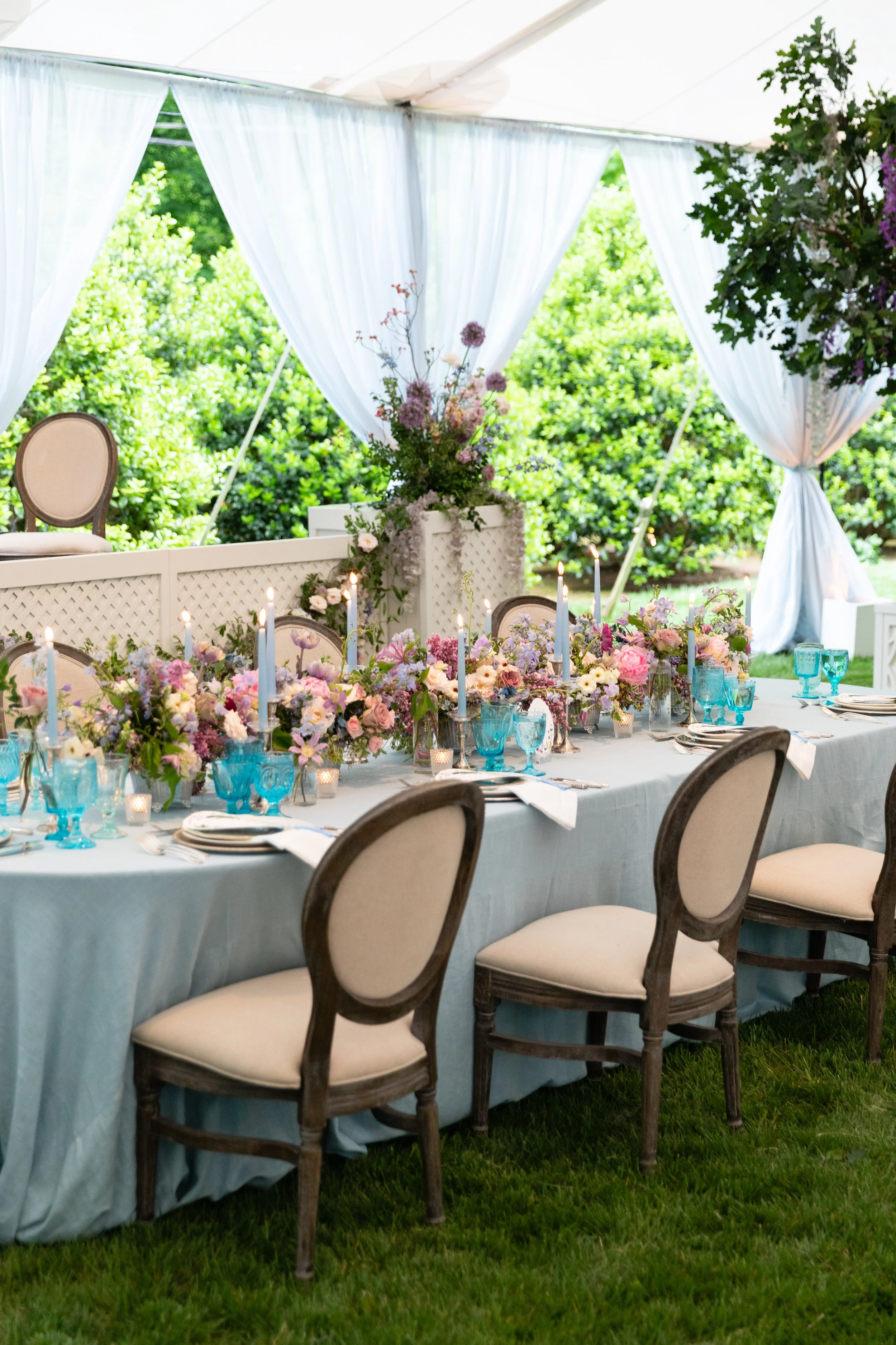 Growing, fresh floral centerpieces with blush garden roses, lilac, blue sweet peas, ranunculus, lavender delphinium, globe allium, and natural greenery for a tented Bridgerton inspired engagement party at a private home in Nashville, TN. Flower by Te