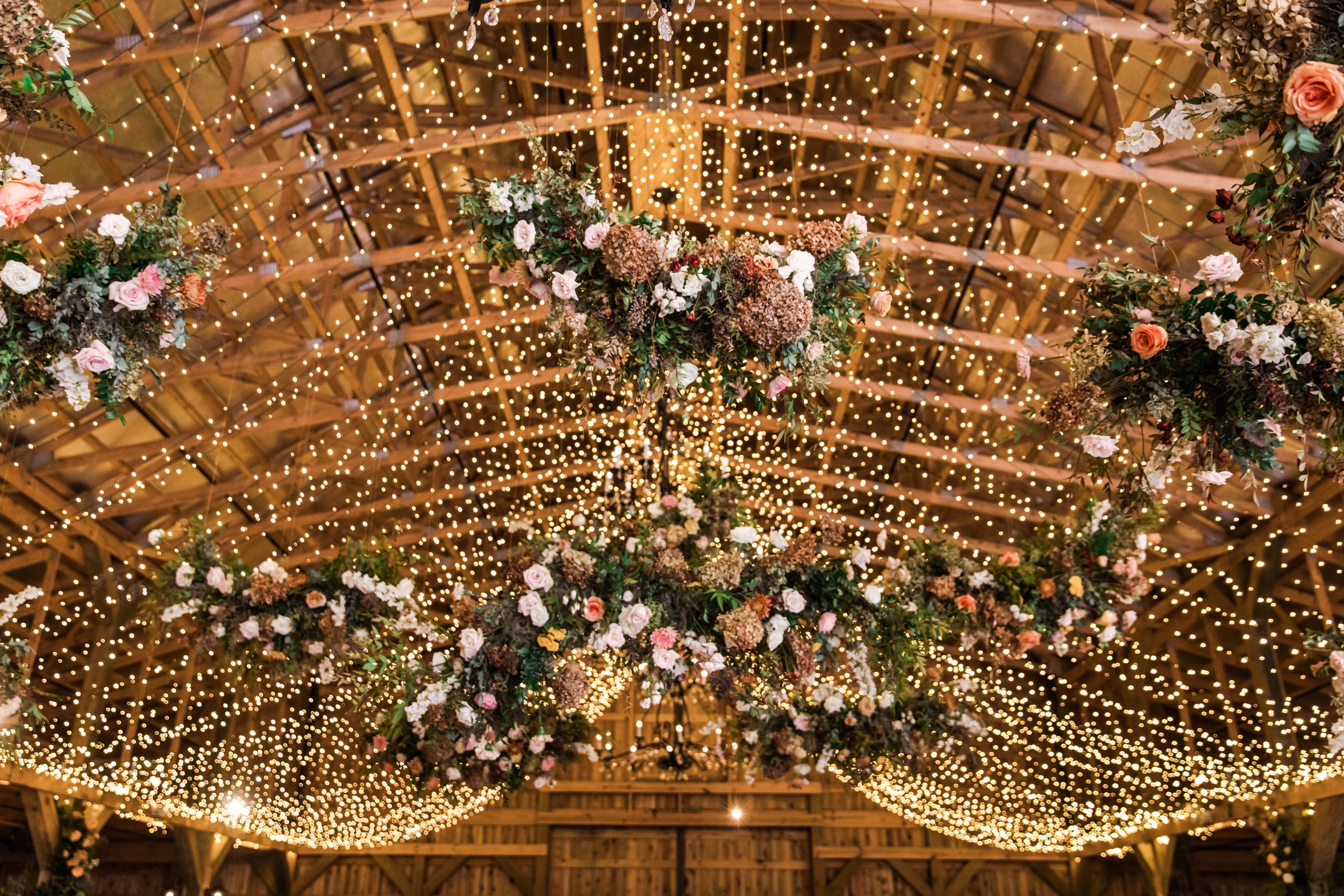 Gorgeous autumnal floral clouds hang over the dance floor, including terra cotta, rose gold, toffee, blush, and neutral florals. These clouds feature lush garden roses, ranunculus, lisianthus, and privet berries. Designed by Rosemary and Finch in Nas