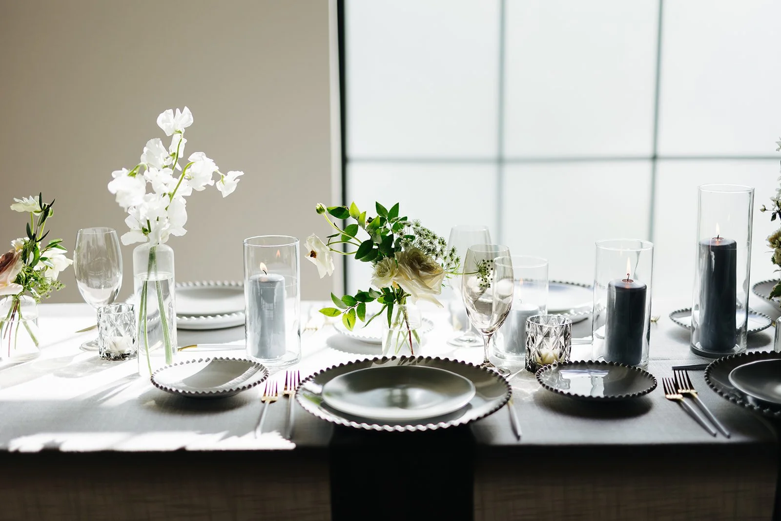 Elegant bud vases with florals of roses, ranunculus, sweet peas, Queen Anne’s lace, butterfly ranunculus in hues of white, cream and blush. Accented with dusty blue tapers and clear glass votives. Designed by Rosemary and Finch in Nashville, TN.