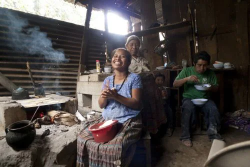 A Guatemalan family sharing the cooking and eating of a meal in a typical Guatemalan house.