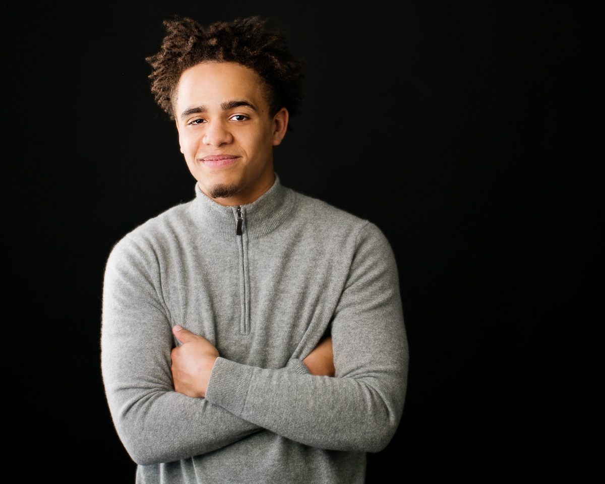  High school senior picture of a young man standing in front of a black background, photographed by the Portland high school senior photographers at Campbell Salgado Studio in Portland, Oregon 