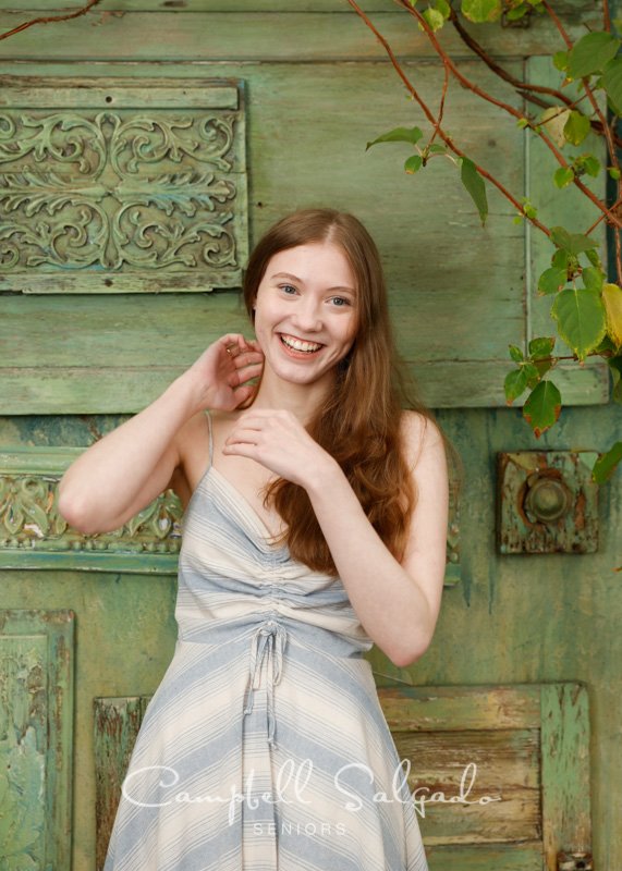  Senior picture of a young woman on vintage green doors background by high school senior portraits photographers at Campbell Salgado Studio in Portland, Oregon. 