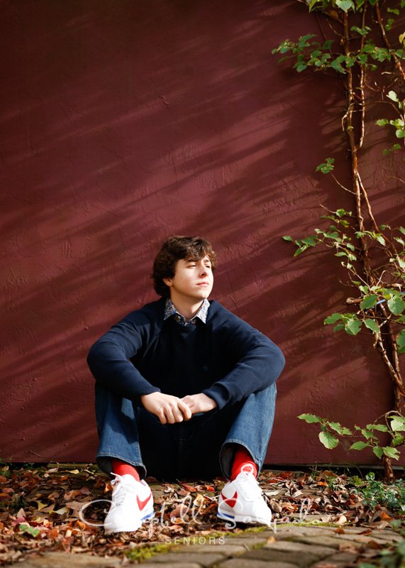  Senior portraits outside of a young man in front of a plum stucco background by high school senior picture photographers photographers at Campbell Salgado Studio in Portland, Oregon. 