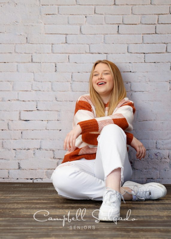  Professional senior portraits of young woman in front of an ivory brick background by Portland, Oregon photographers at Campbell Salgado Studio. 