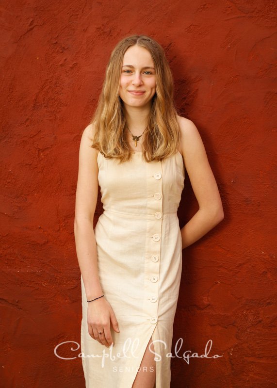  Senior picture of a young woman on a red stucco background by high school senior photographers at Campbell Salgado Studio in Portland, Oregon. 