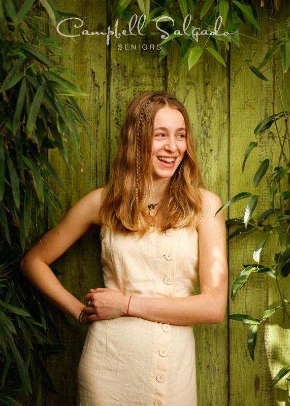  Senior pictures outside of a young woman in front of a lime fenceboards background by high school senior portrait photographers photographers at Campbell Salgado Studio in Portland, Oregon. 