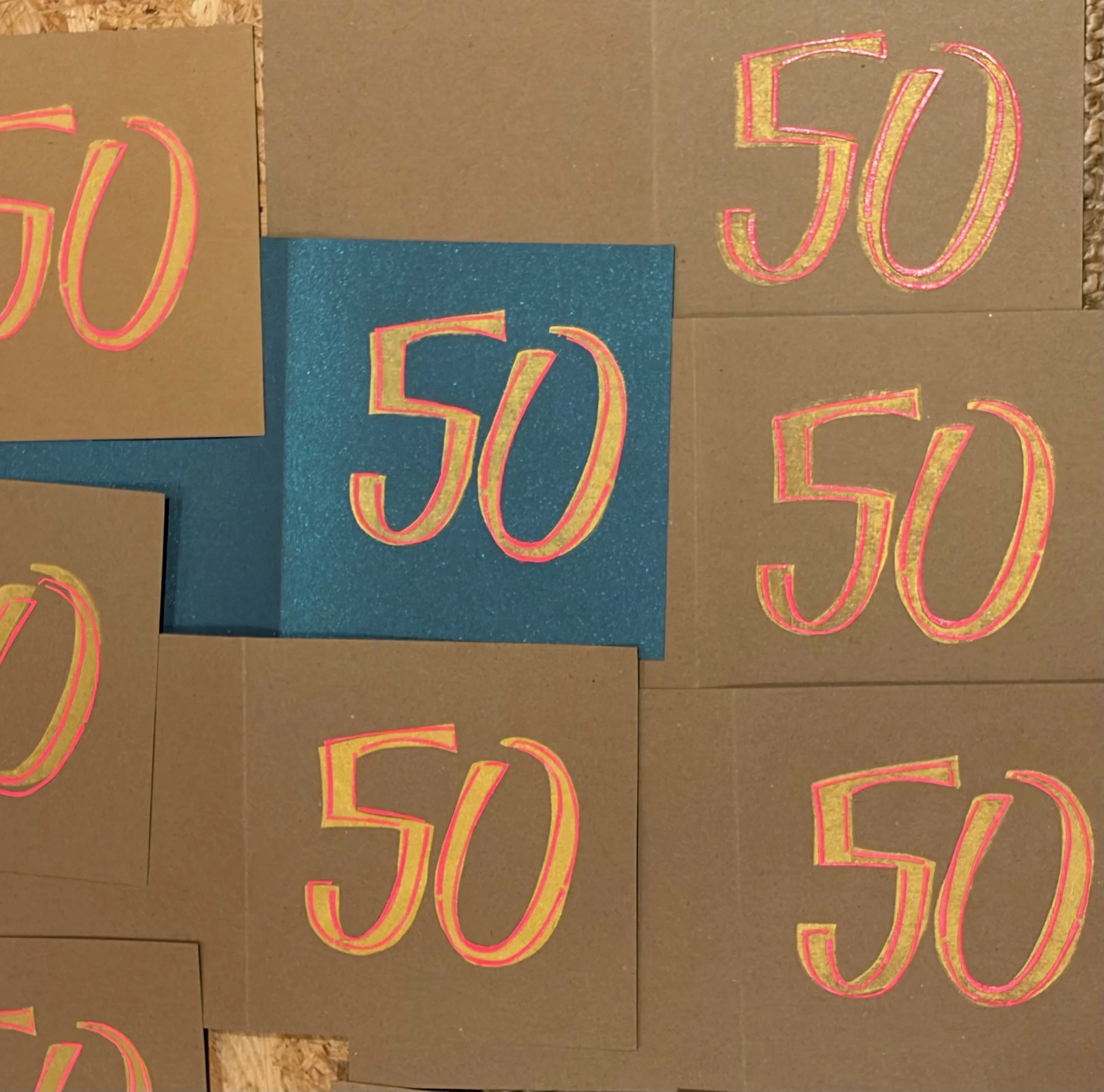 Close-up of decorated cards with the number 50 outlined in pink and gold, on a surface of brown and blue-colored background.