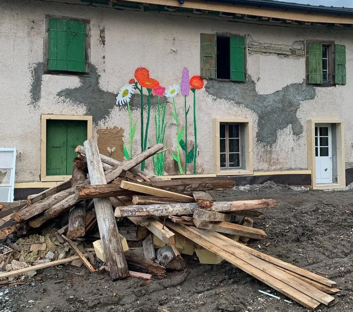 A building with a large colorful mural of flowers painted on its weathered wall, with broken wooden construction debris on the ground in front.