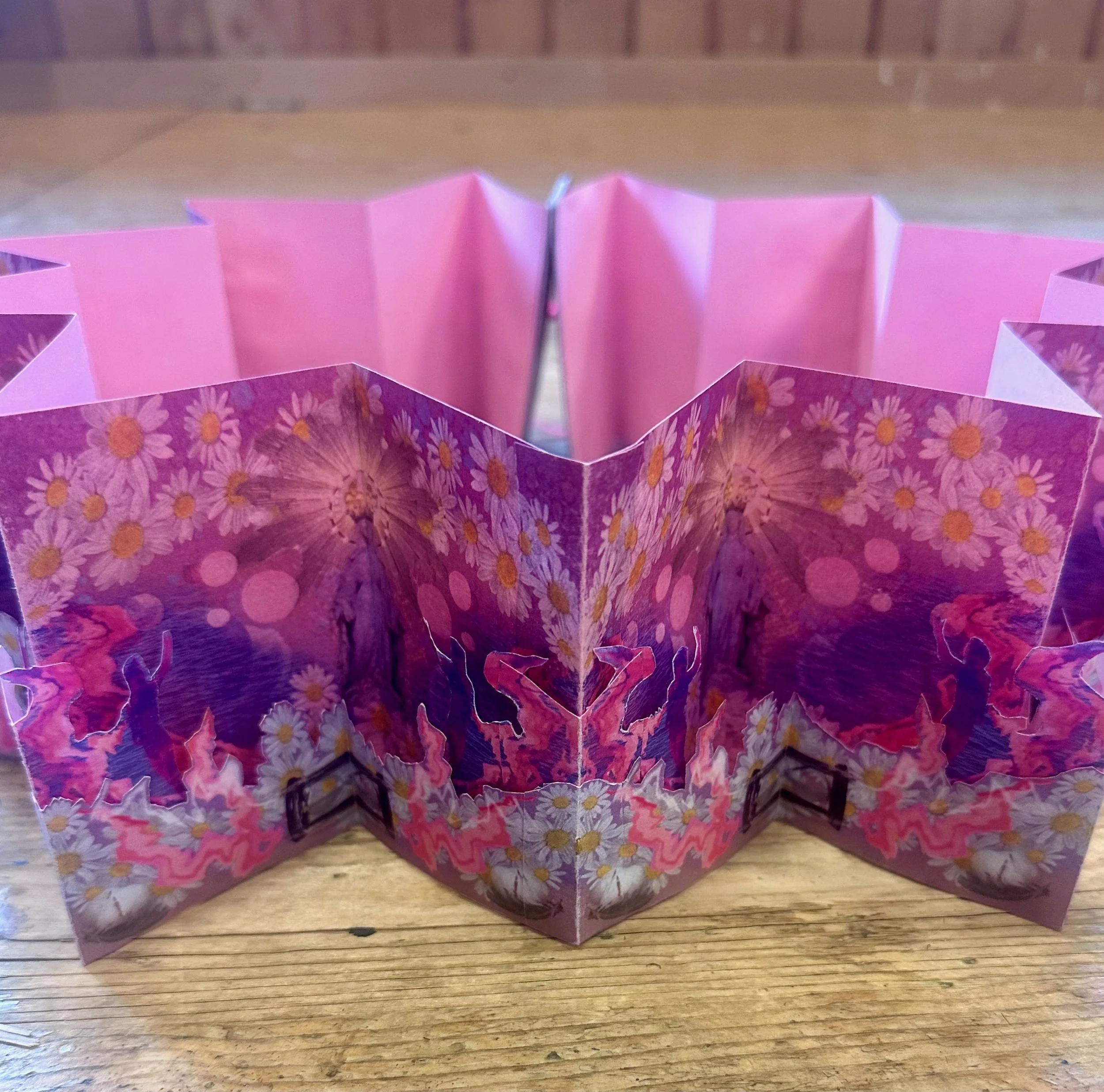 A paper craft with pink and purple floral patterns, folded into a star and butterfly shapes, placed on a wooden surface.