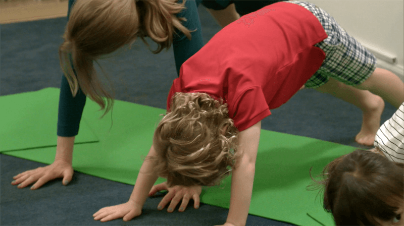 Children practicing downward facing dog yoga pose in a classroom