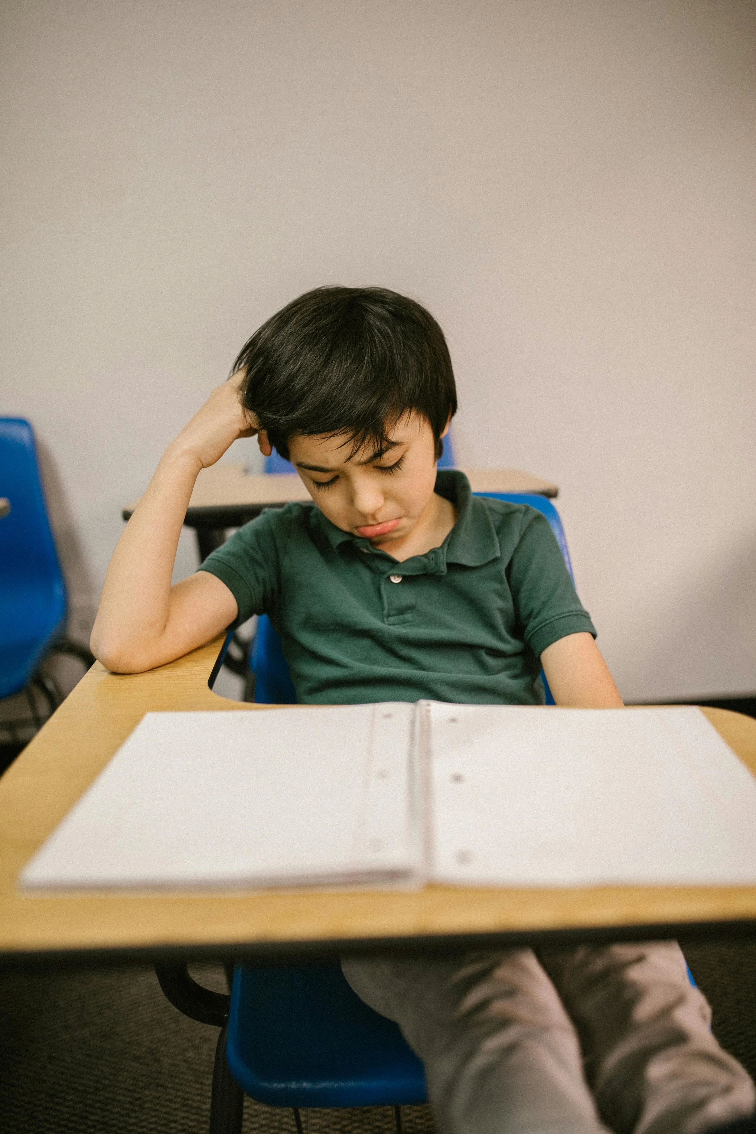 Sad student sitting at desk with with his head in his hands, looking at a blank notebook