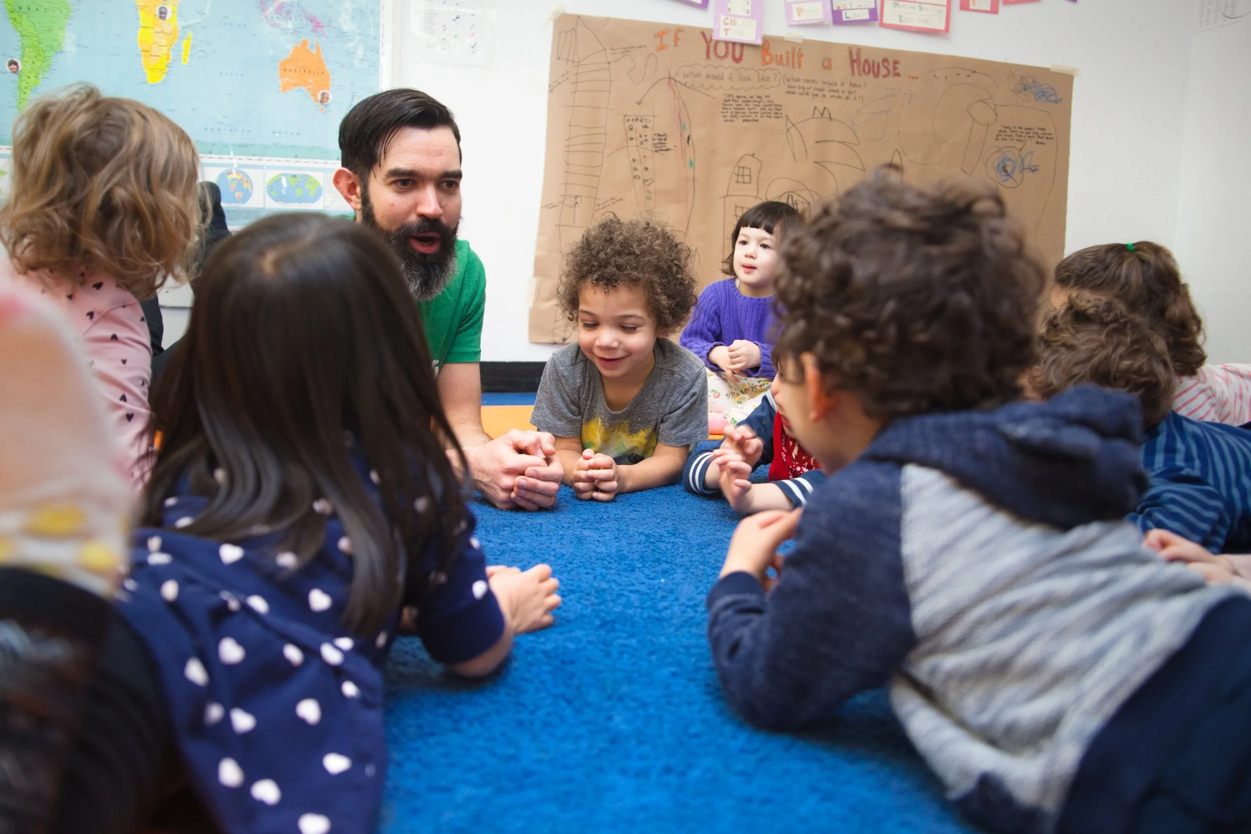 A teacher smiles and talks with a group of students in cobra pose as they do a classroom yoga break.