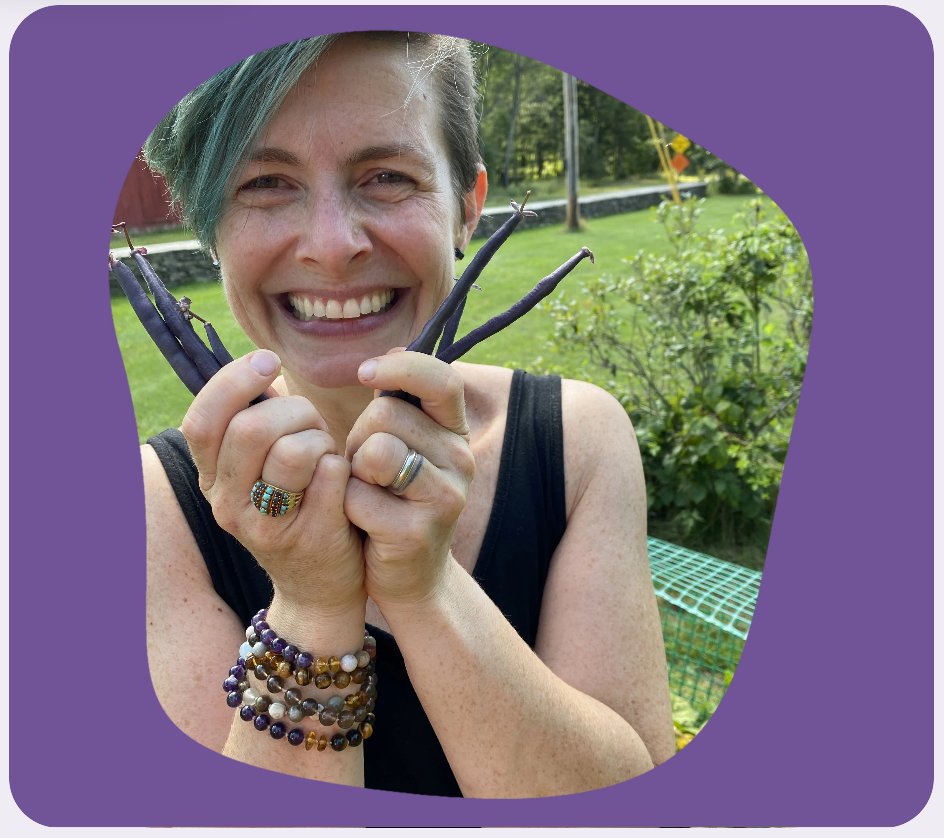 Rachel Costello outside in a garden holding up purple beans and smiling.
