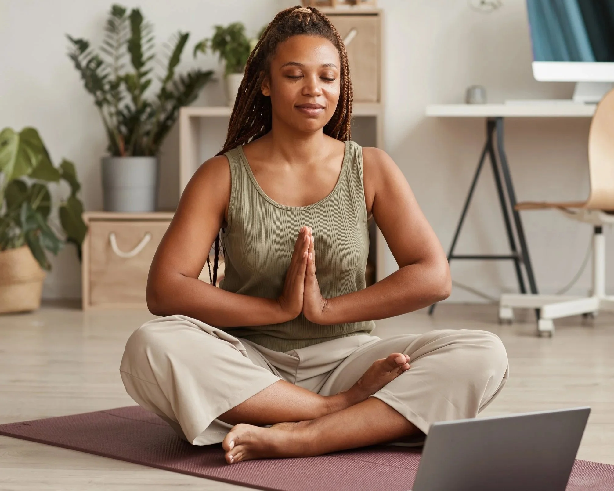 Woman sitting cross-legged on a yoga mat with palms together and eyes closed. Online yoga teacher training.