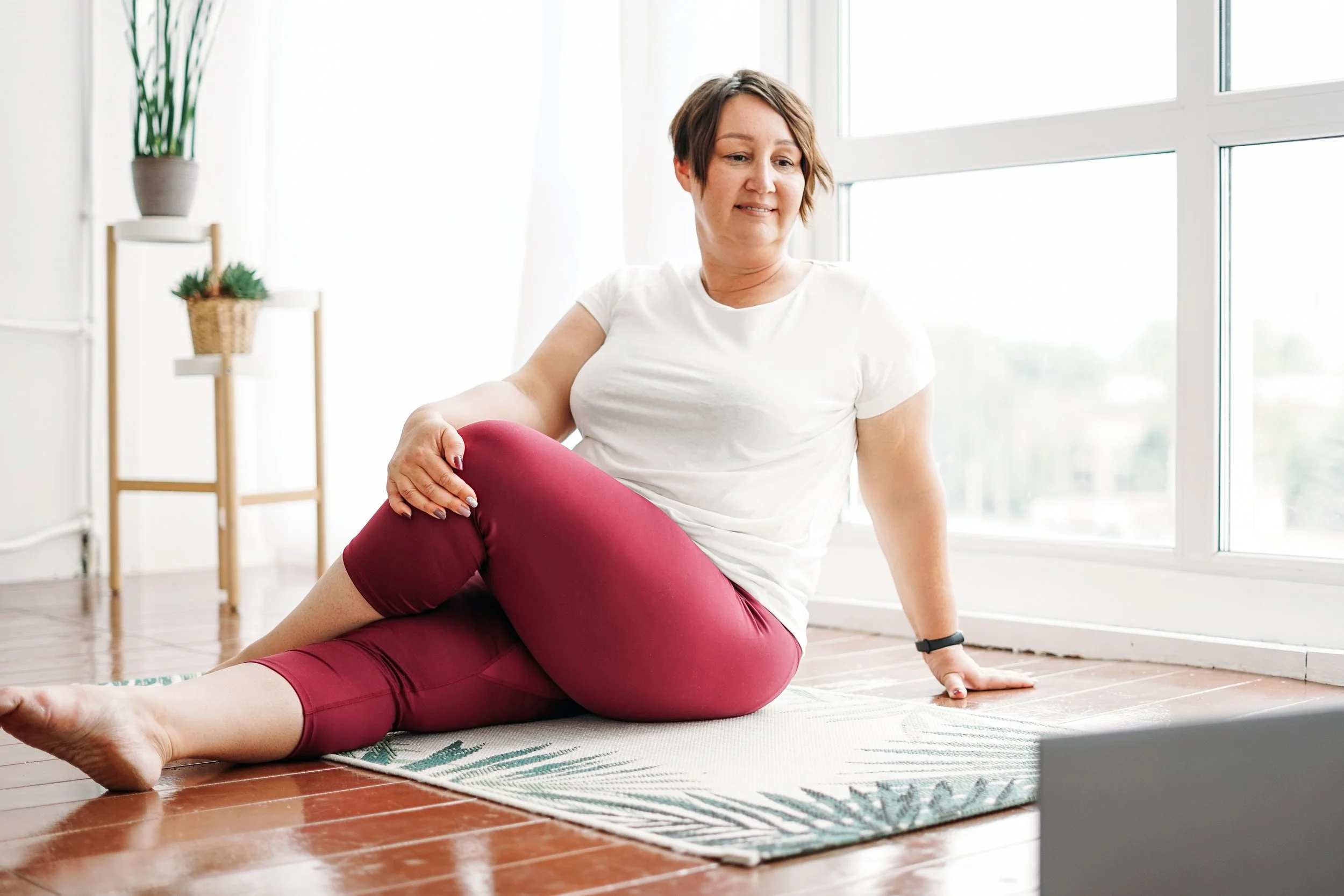 Woman in a yoga pose looking at her computer in a bright sunny room.