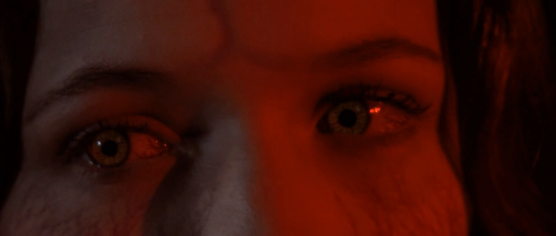 Close-up of a person's face illuminated by a red light, showing their eyes and eyebrows.