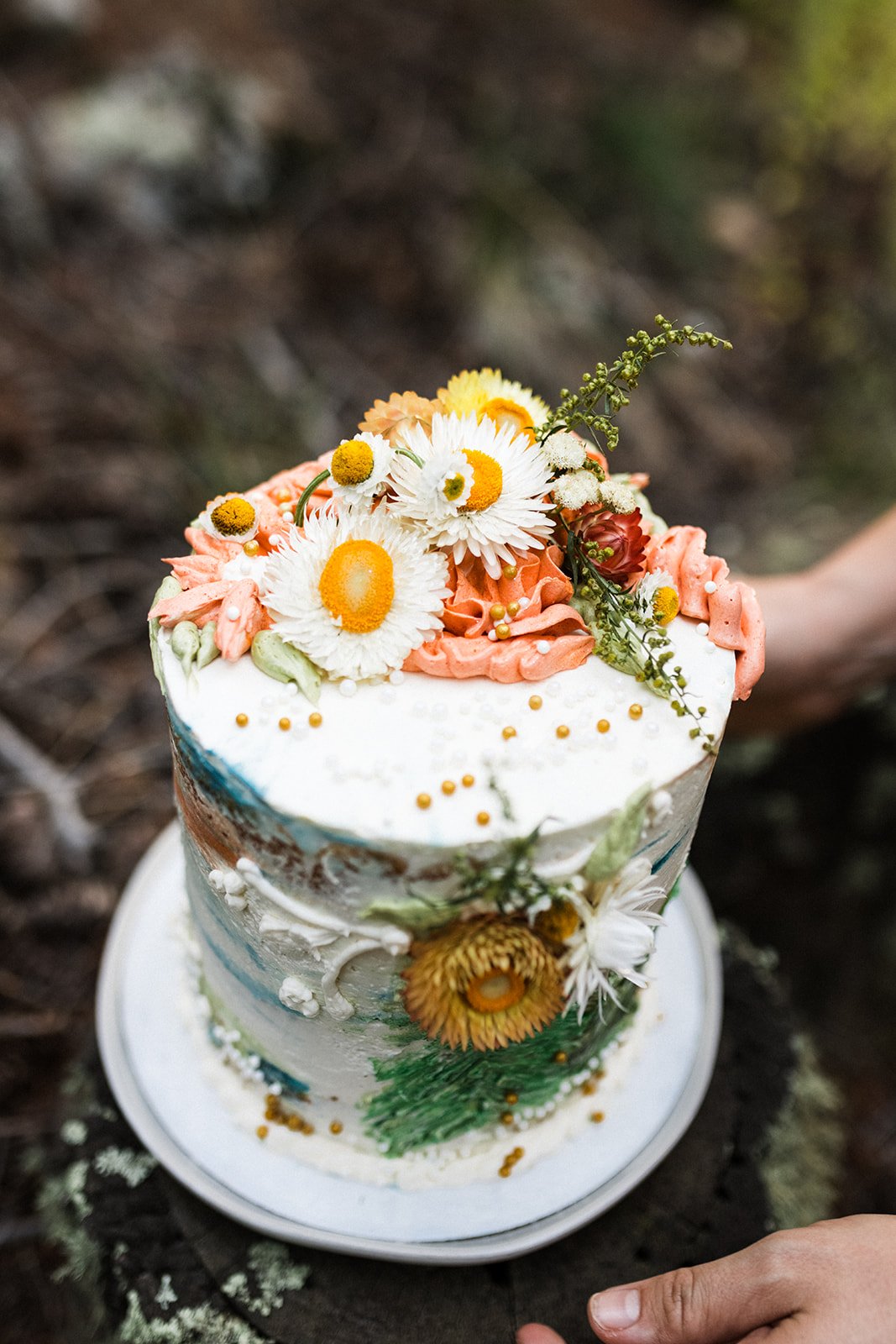  Photo of a floral naked wedding cake for an intimate mountain elopement. The cake is decorated with florals in buttercream with gold beads and assorted daisies in white and gold. 