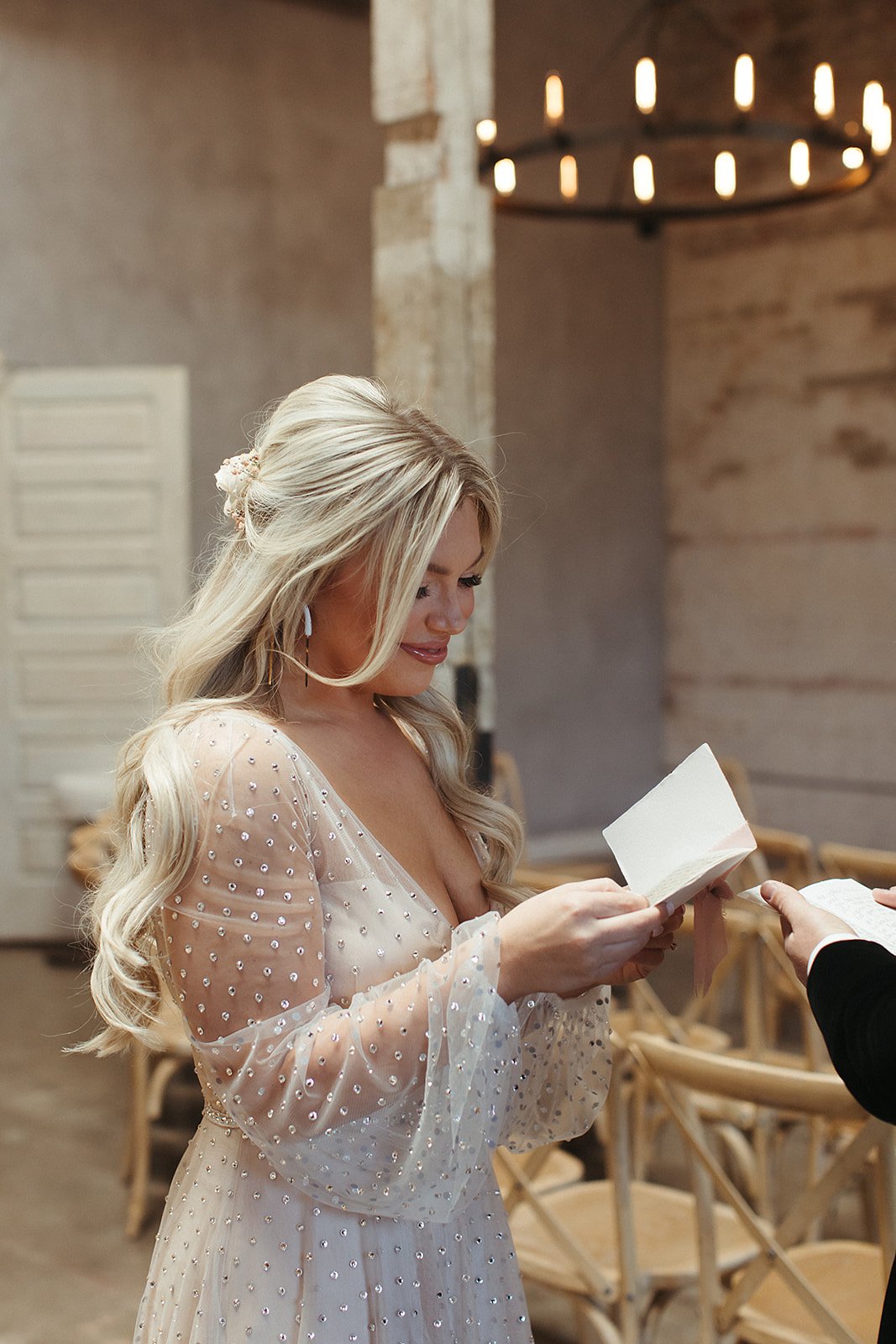  A bride wearing Lunella by Willowby by Watters with long blond hair in soft curls, reading a note from the groom during the couple’s first look. 