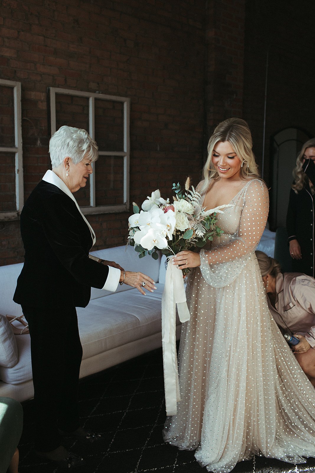  A bride wearing Lunella by Willowby by Watters wedding dress, showing off her large white bridal bouquet with orchids and silk ribbon to her grandmother. 