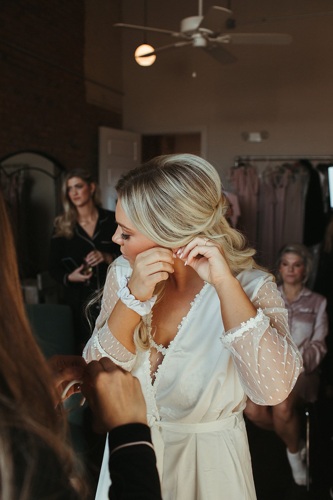  A bride wearing a white silk lace robe getting ready on their wedding day surrounded by bridemaids. 