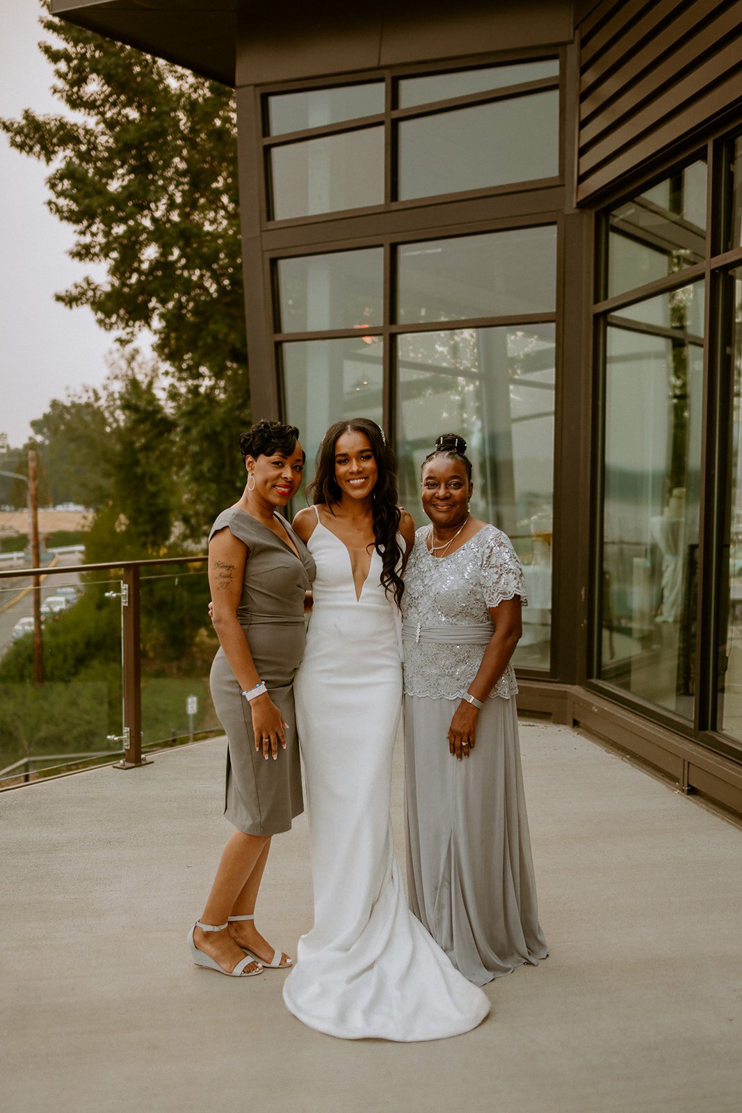  A bride wearing TENNYSON by The Label, a deep v neck illusion fitted crepe wedding dress. The bride is posing for a photograph with family after the couple’s waterside ceremony in Washington. 