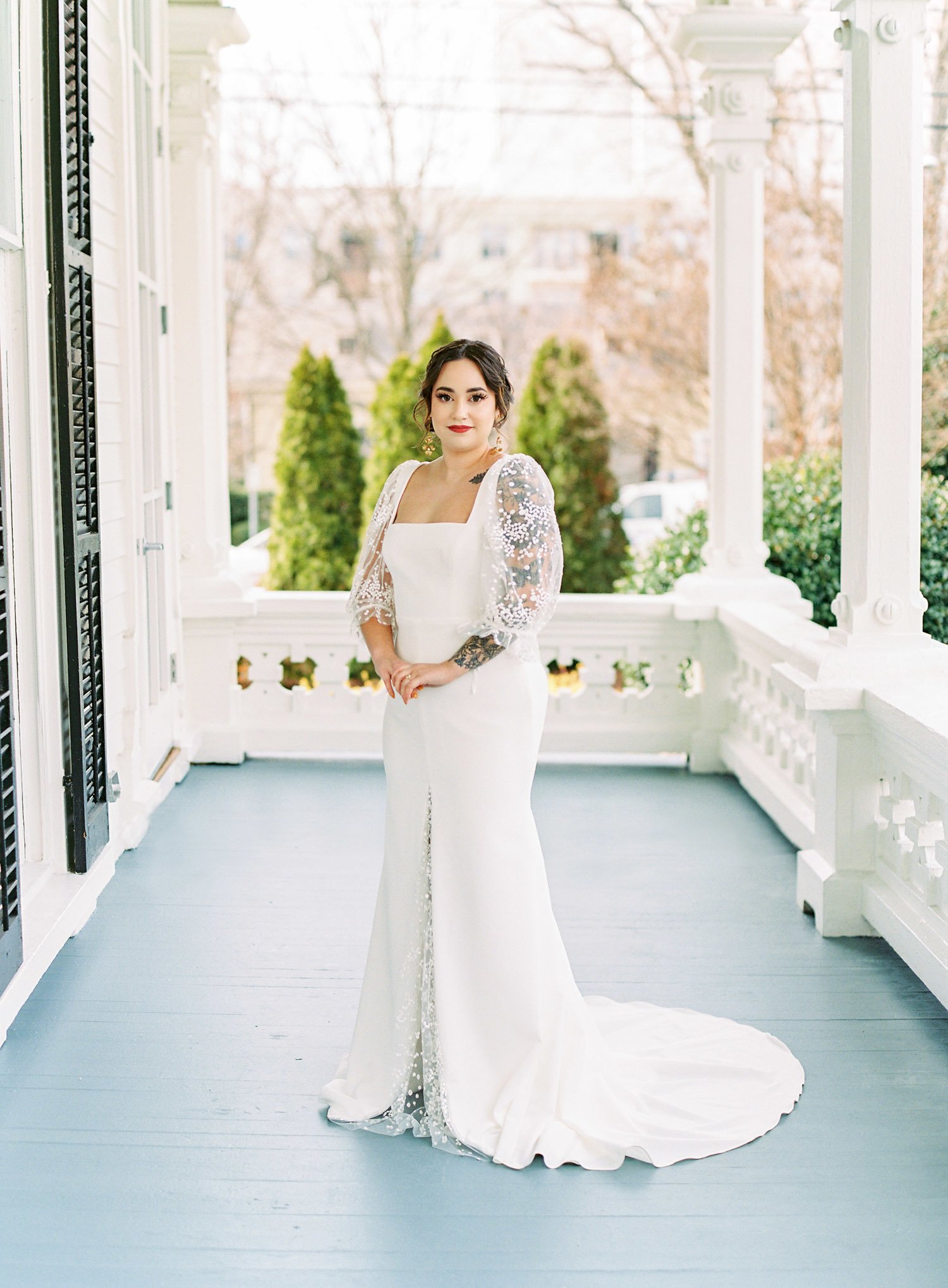  'florence' wedding dress by laudae bridal, a square neck fitted crepe bridal gown with sheer lace puff sleeves and a low back, photographed on the porch of the merrimon-wynne house in raleigh, north carolina    