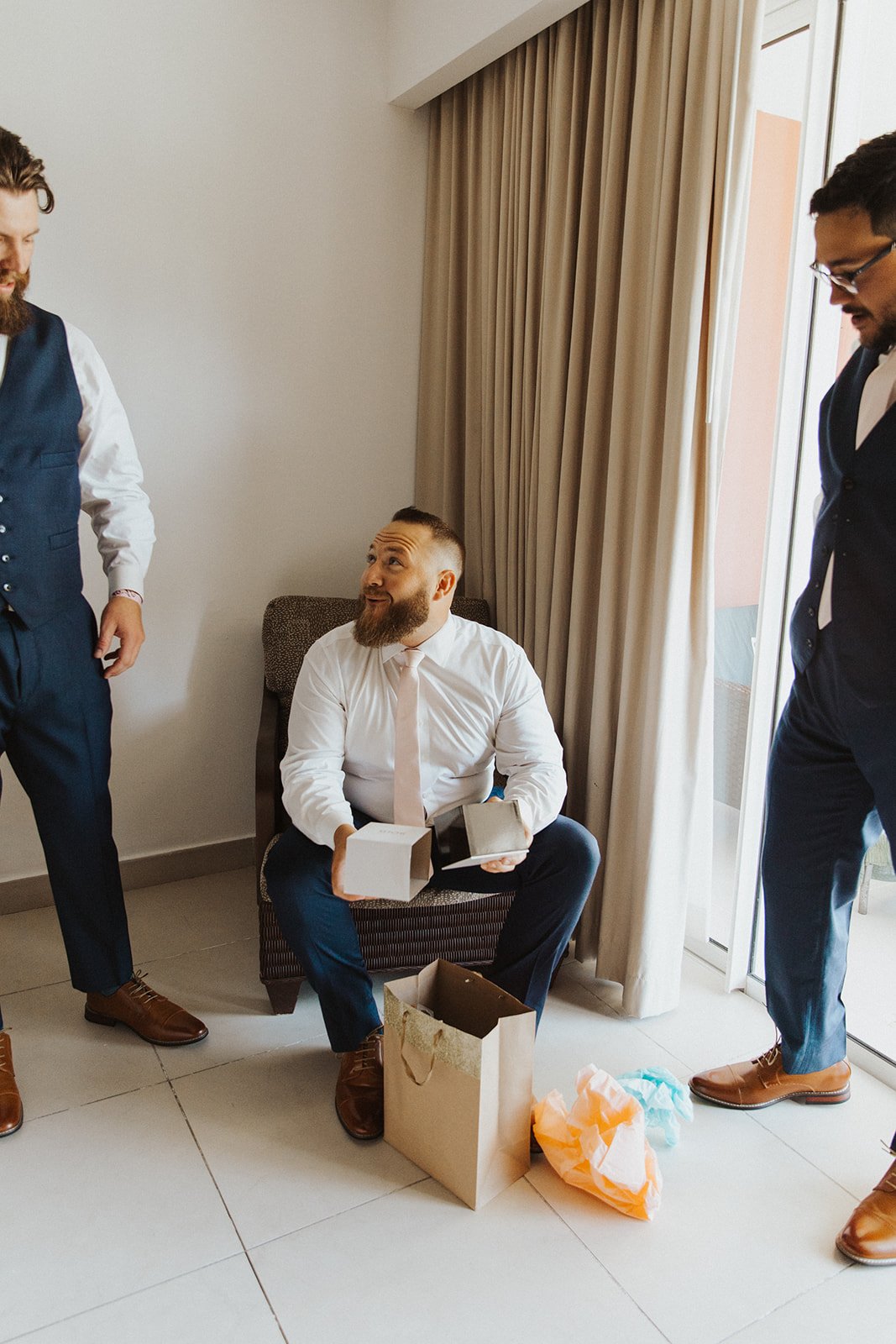  A groom getting ready for a wedding ceremony opening gifts and laughing with friends. 