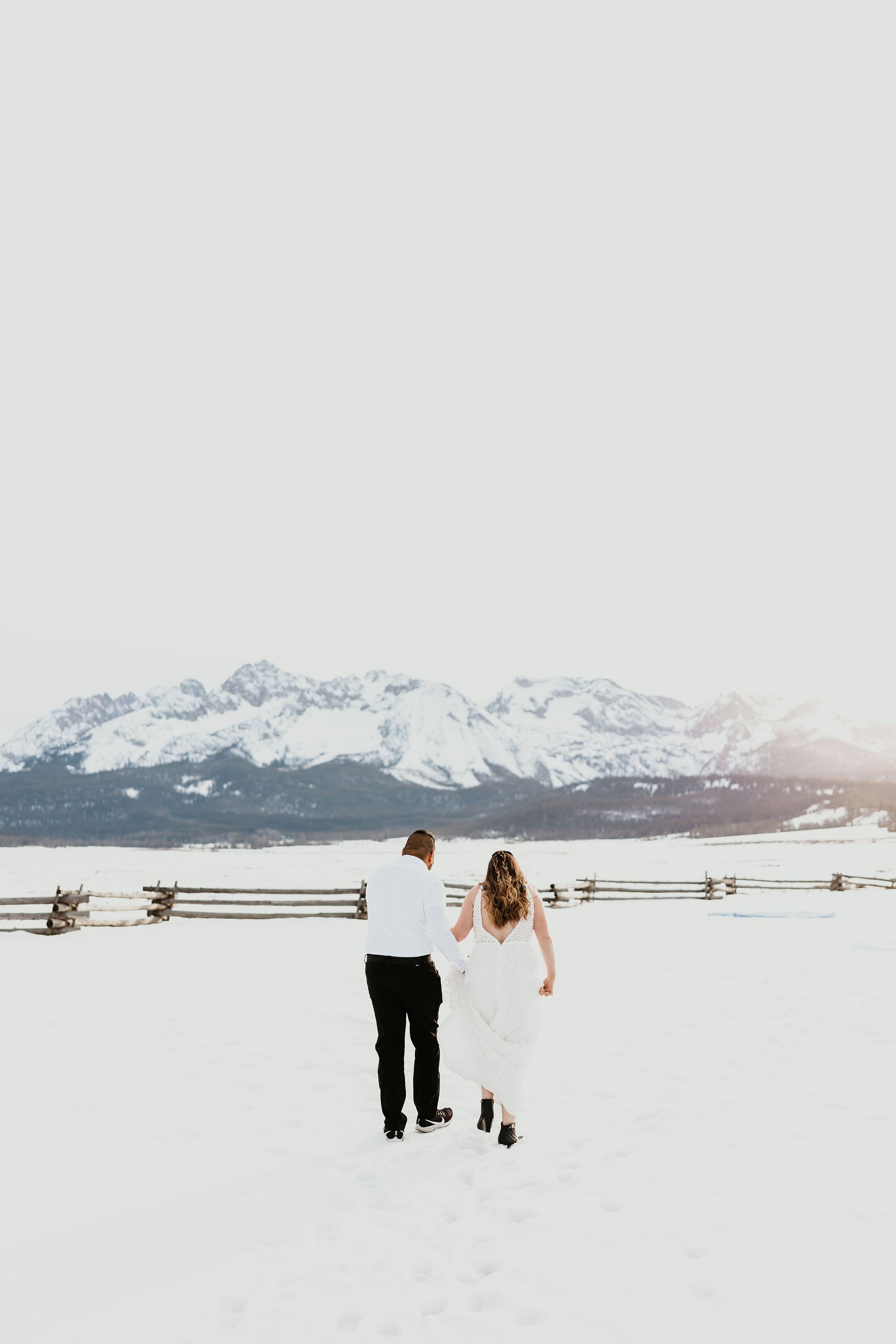  a bride wearing the ‘Louie’ wedding dress by Made With Love standing in a snowy field in the mountains of Idaho holding hands with the groom 