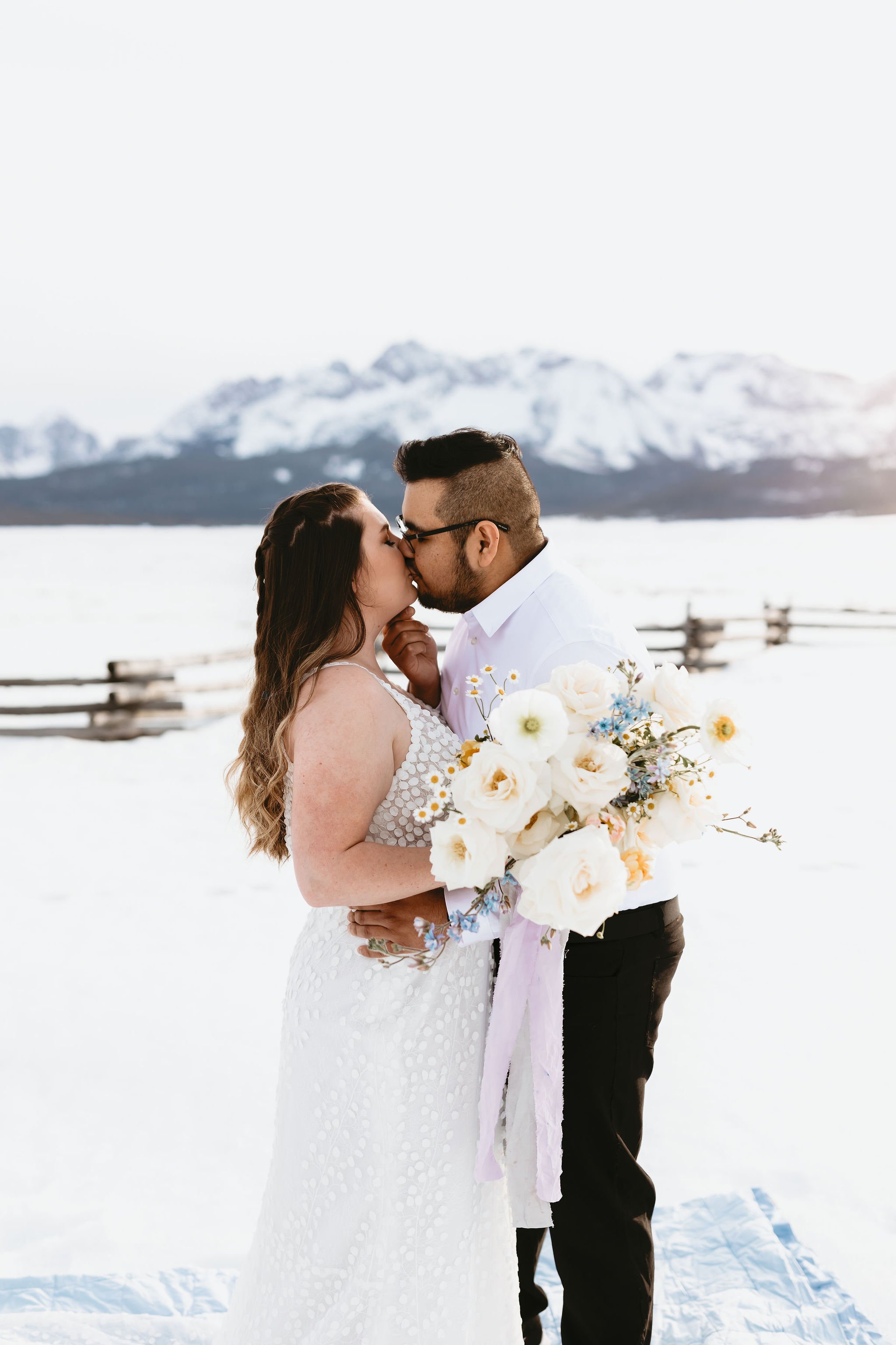  A bride and groom exchanging a kiss for their snowing mountain elopement in Idaho. The bride is wearing Made With Love ‘Louie’ wedding dress from a&amp;bé bridal shop in Boise. 