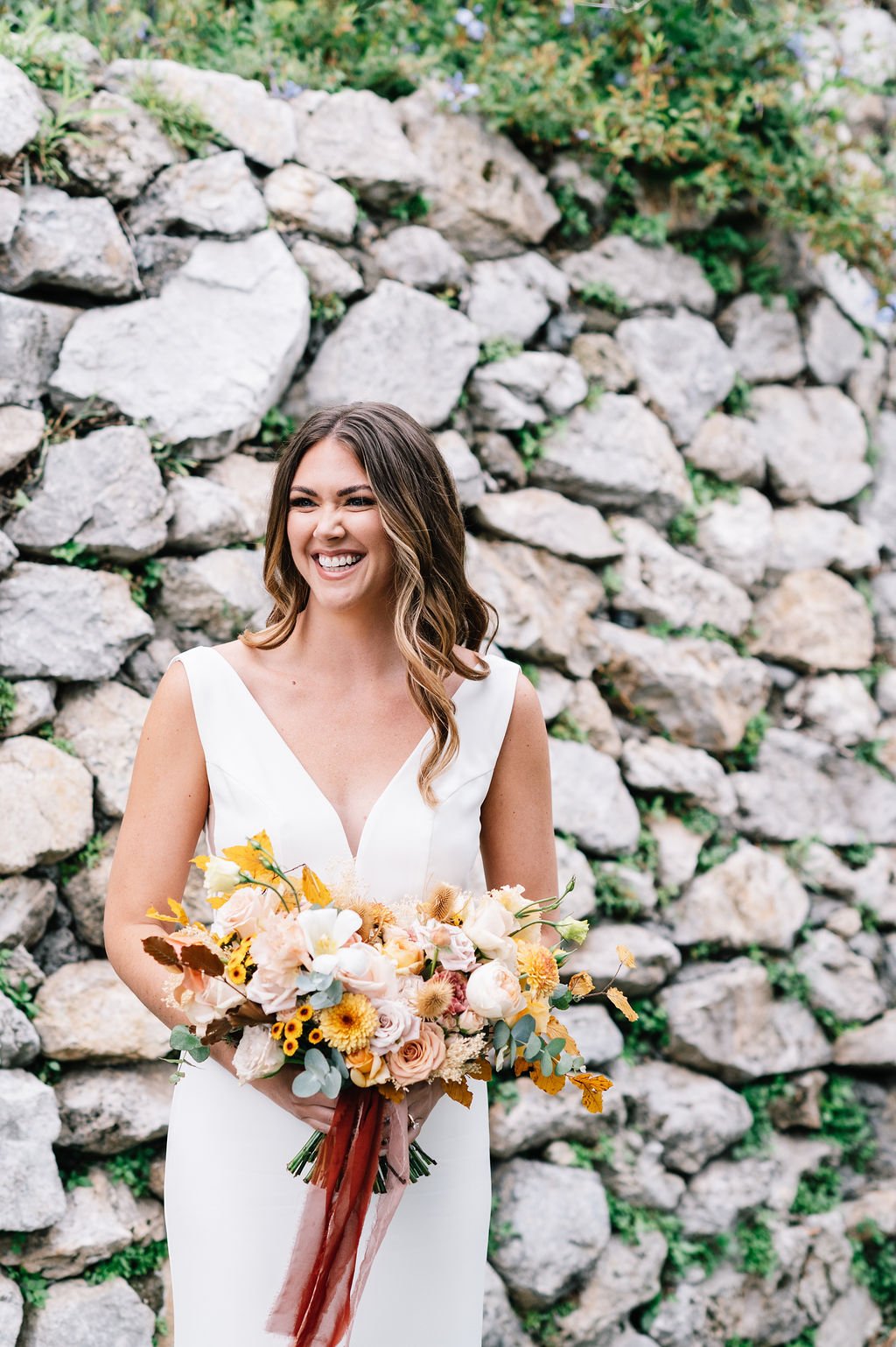 a happy bride in a simple crepe made with love wedding dress holding a wildflower bouquet