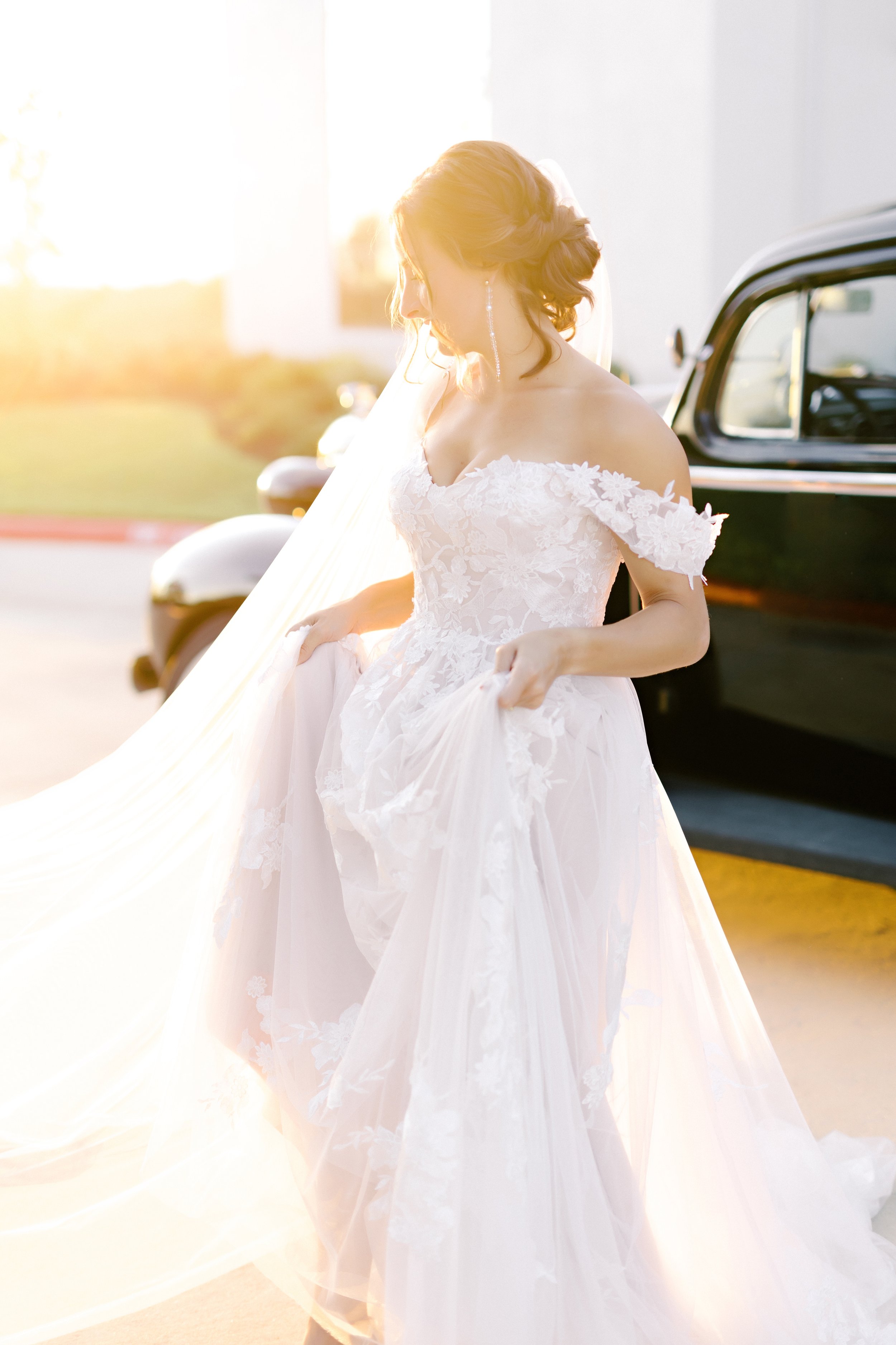 a styled bride wearing an off the shoulder a-line wedding dress in the golden hour leaving the getaway car