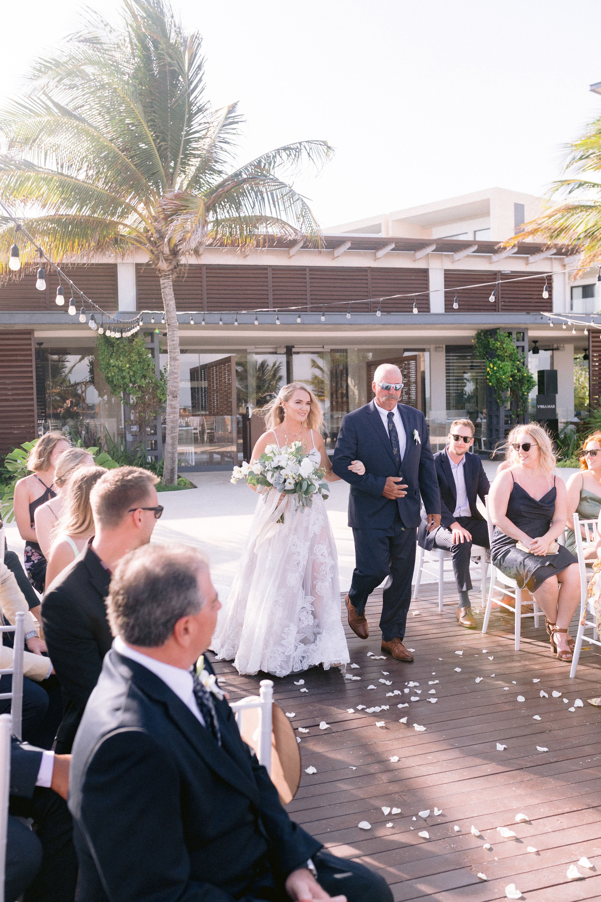 the bride with the father of the bride carring her tropical bouquet in this resort wedding in mexico