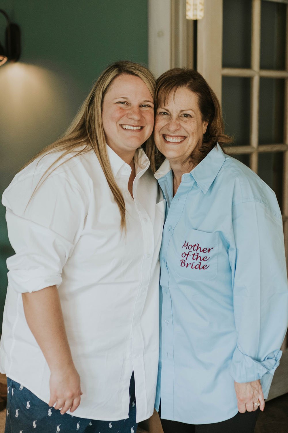  a bride and the mother of the bride embracing and smiling while getting ready  
