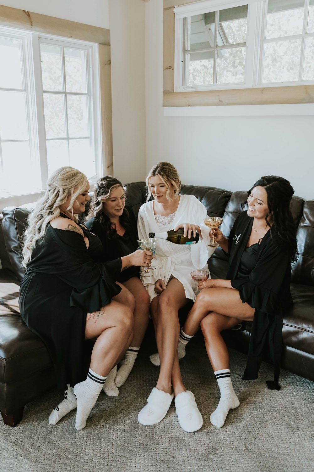  a bridal party in white and black silk robes toasting with champagne while getting ready 