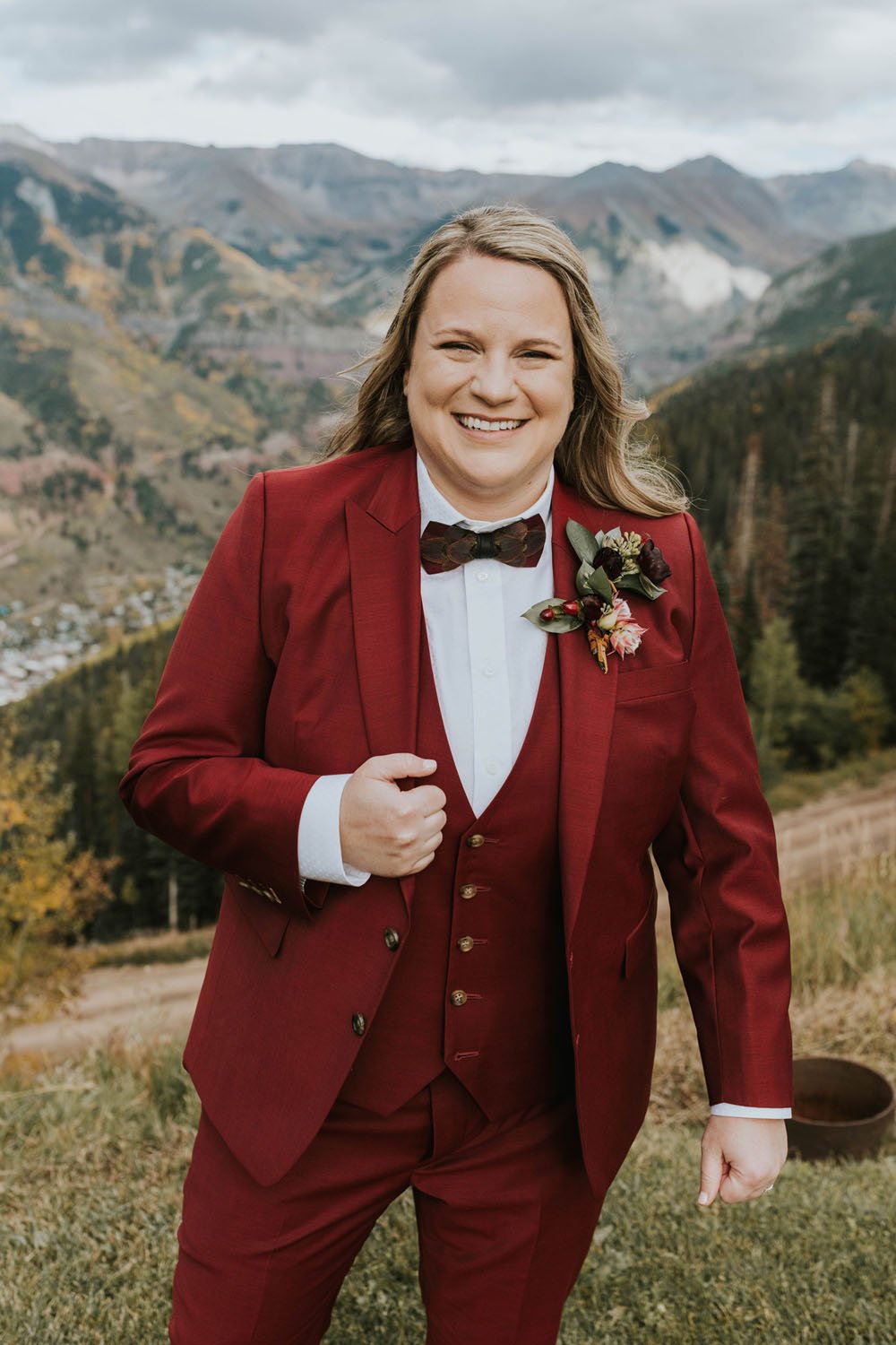  a bride standing on a balcony smiling wearing a lovely burgundy bridal suit  