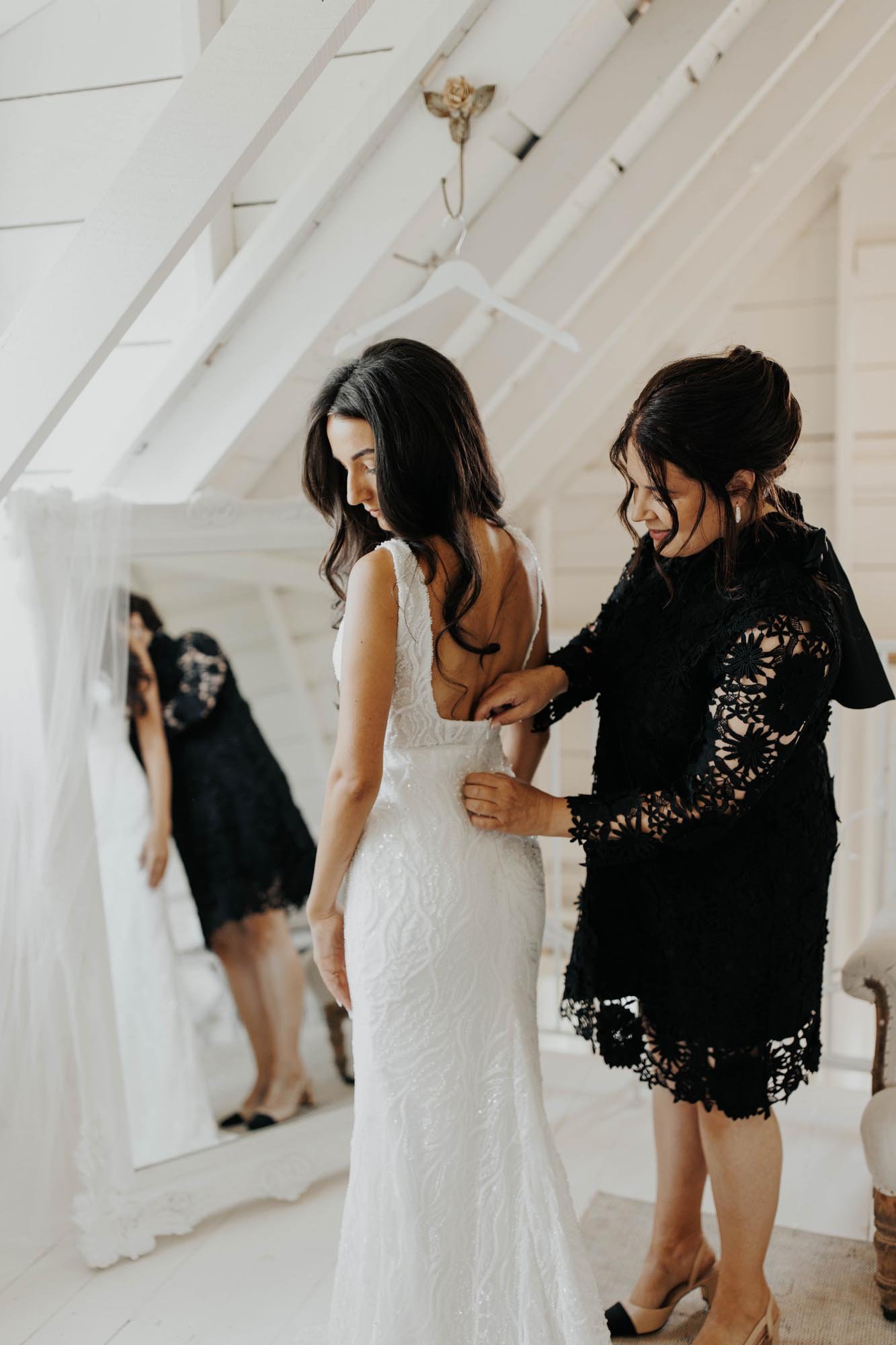  A bride getting ready for her big day while her mother helps zip her into her white beaded wedding dress. 
