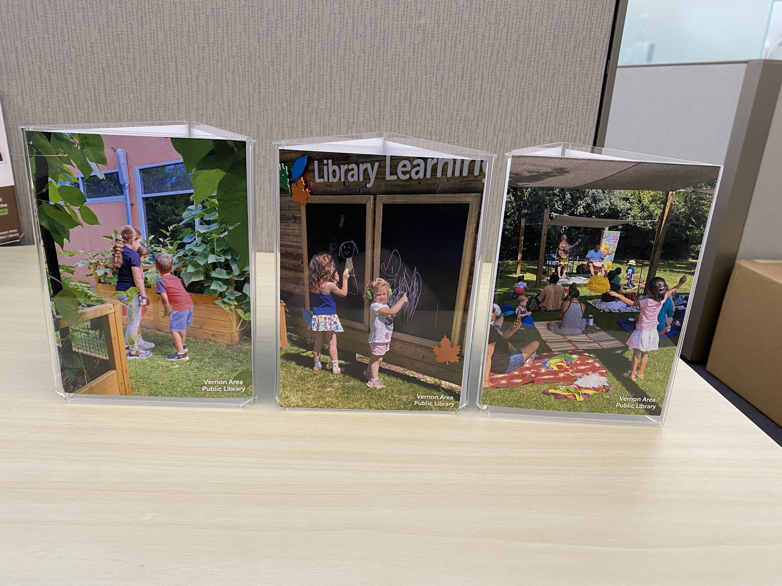 Three tri-sided table signs with phographs of children using the learning garden