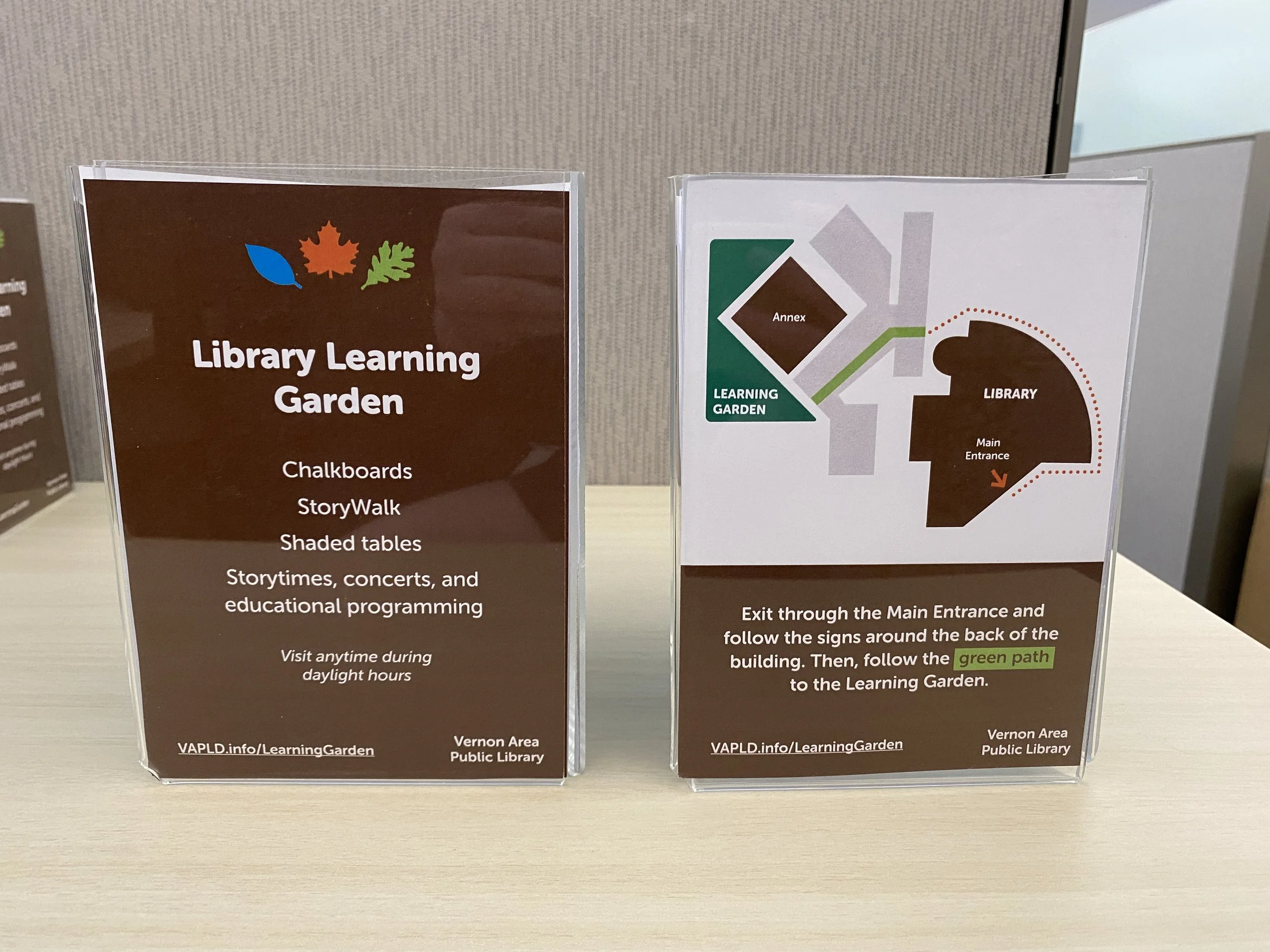 two tri-sided table signs with information about the learning garden