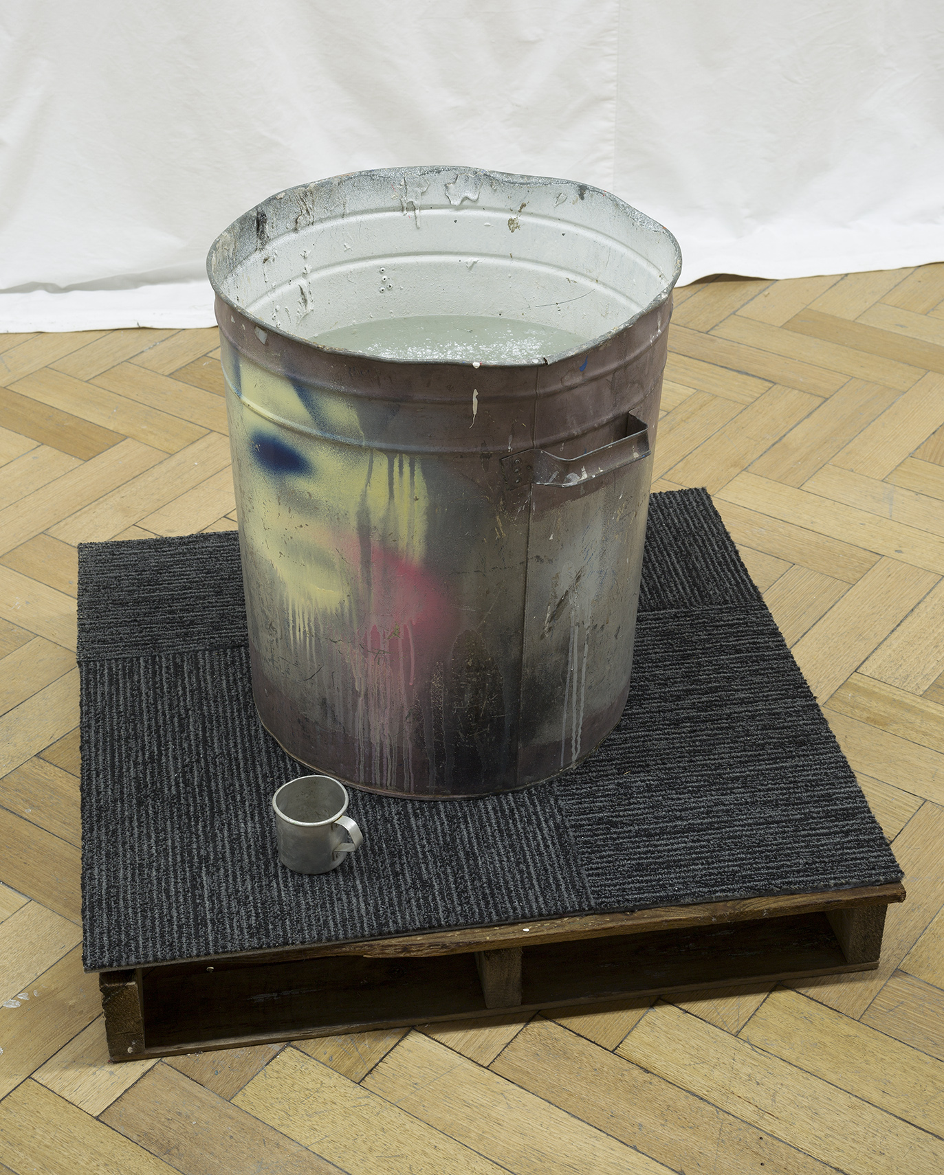   Swish or Swill, 2017. Found tin can, found tin cup, crate, carpet tiling, water and asbestos like talcum powder, 1200 X 900 X 1200 mm. Image: Christian Capurro 