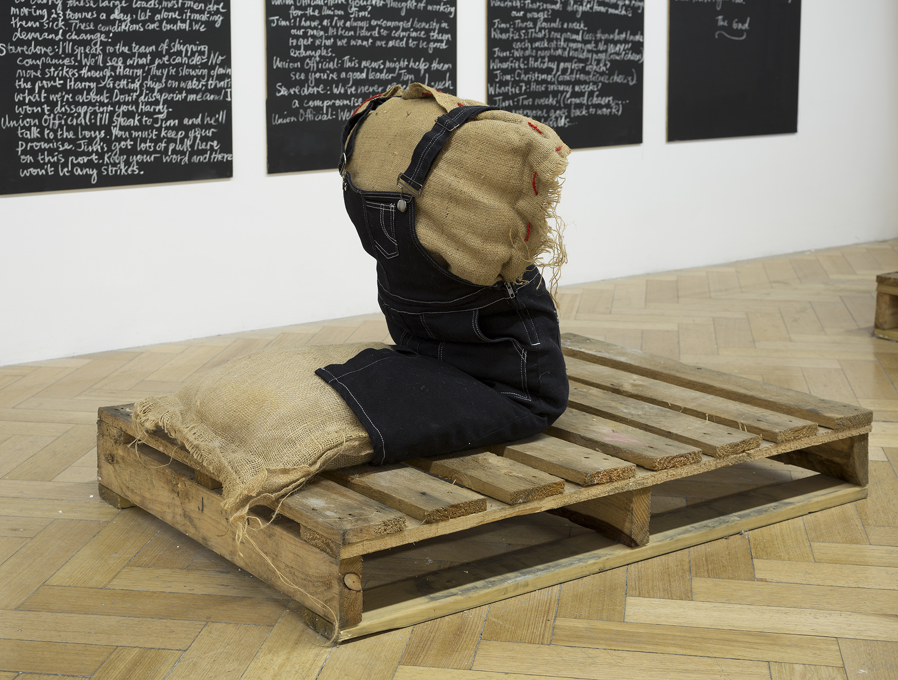   My life as a wharfie learnerar,  2017, hessian sack, and twine wadding and newspaper, purchased girl overall dress, found crate, 810 x 800 x 1010 mm. Image: Christian Capurro. 