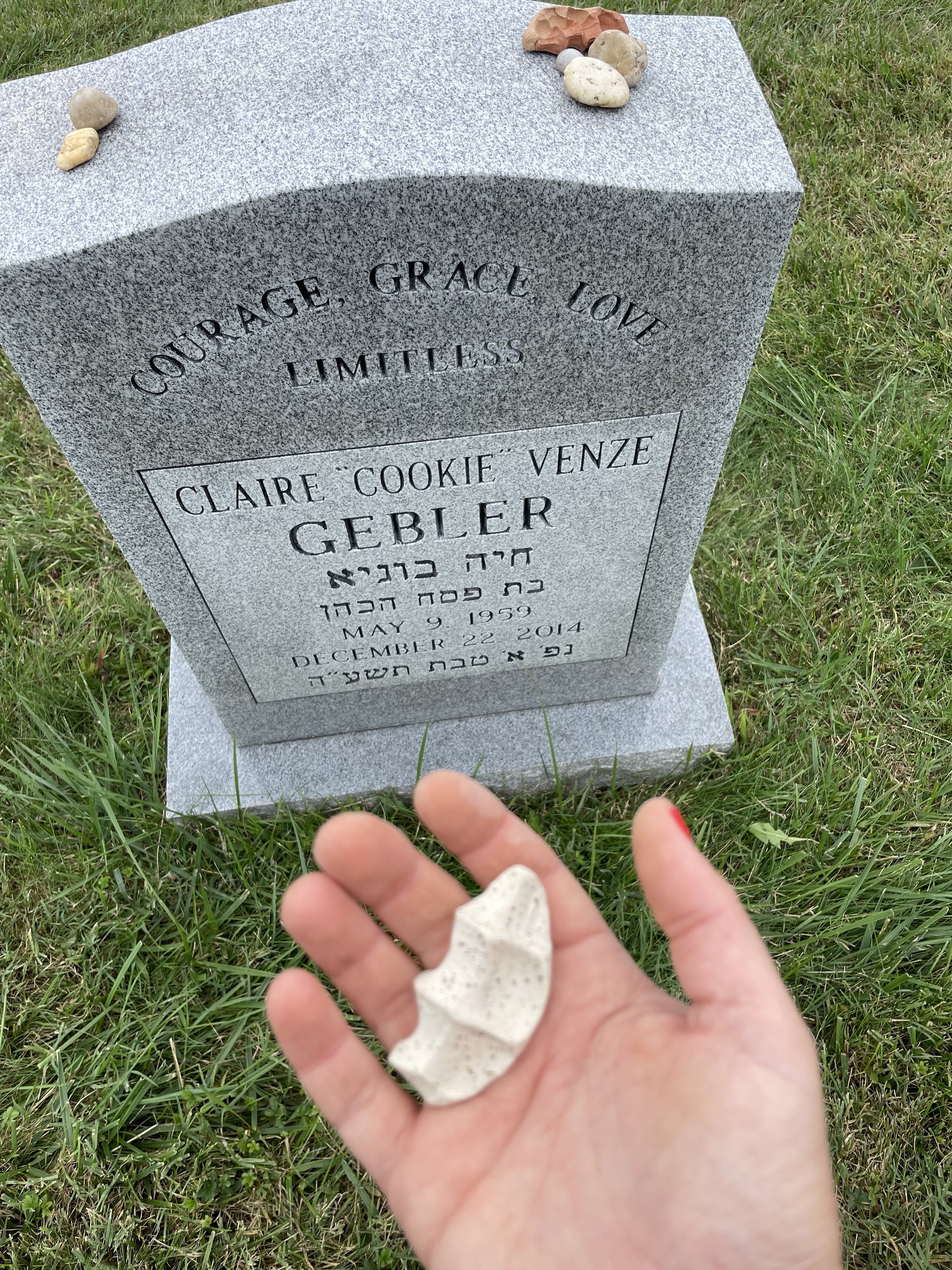 open palm hand holding grief stone in front of headstone at cemetery
