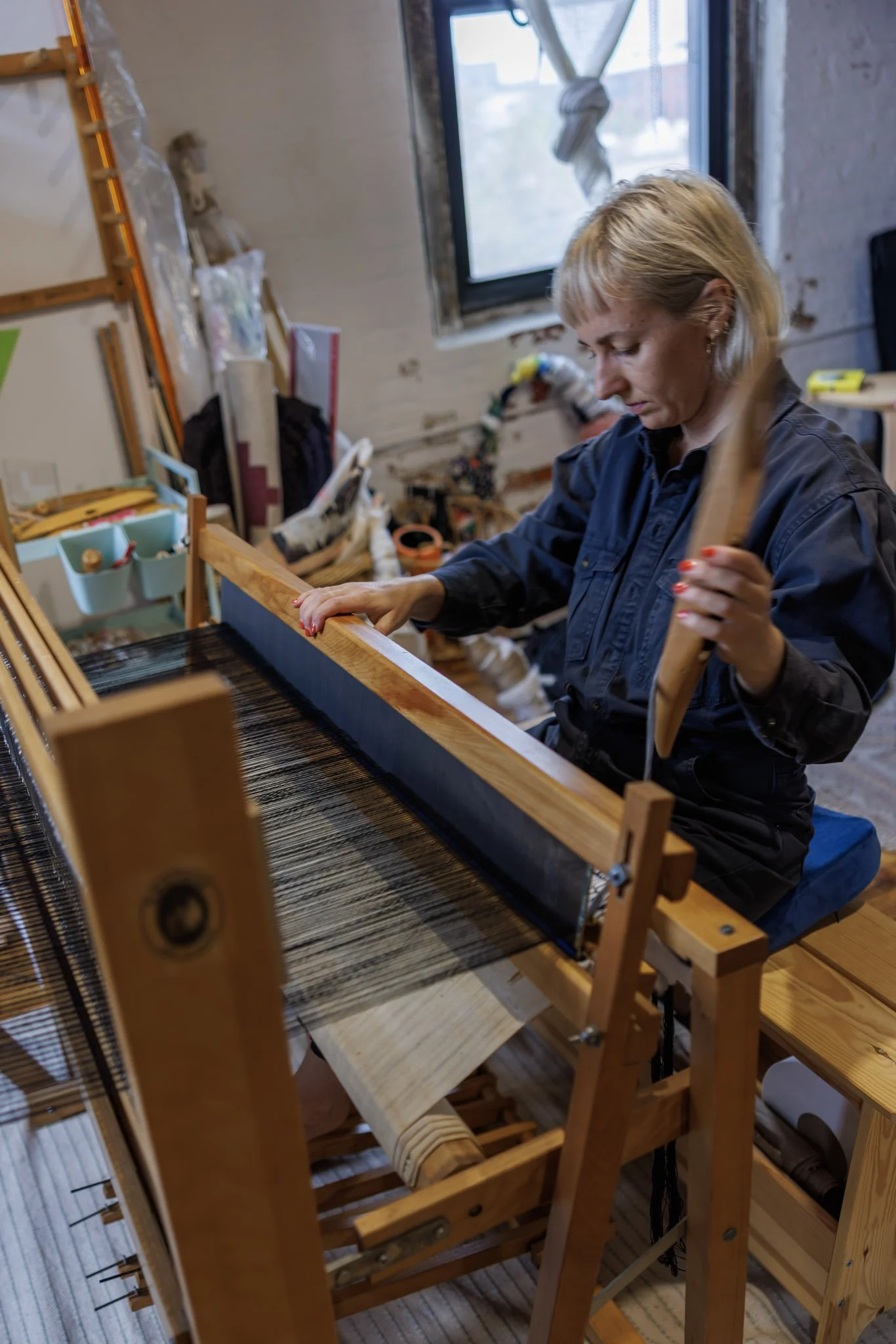 Meirav Ong operating a woven loom in a cozy workshop.