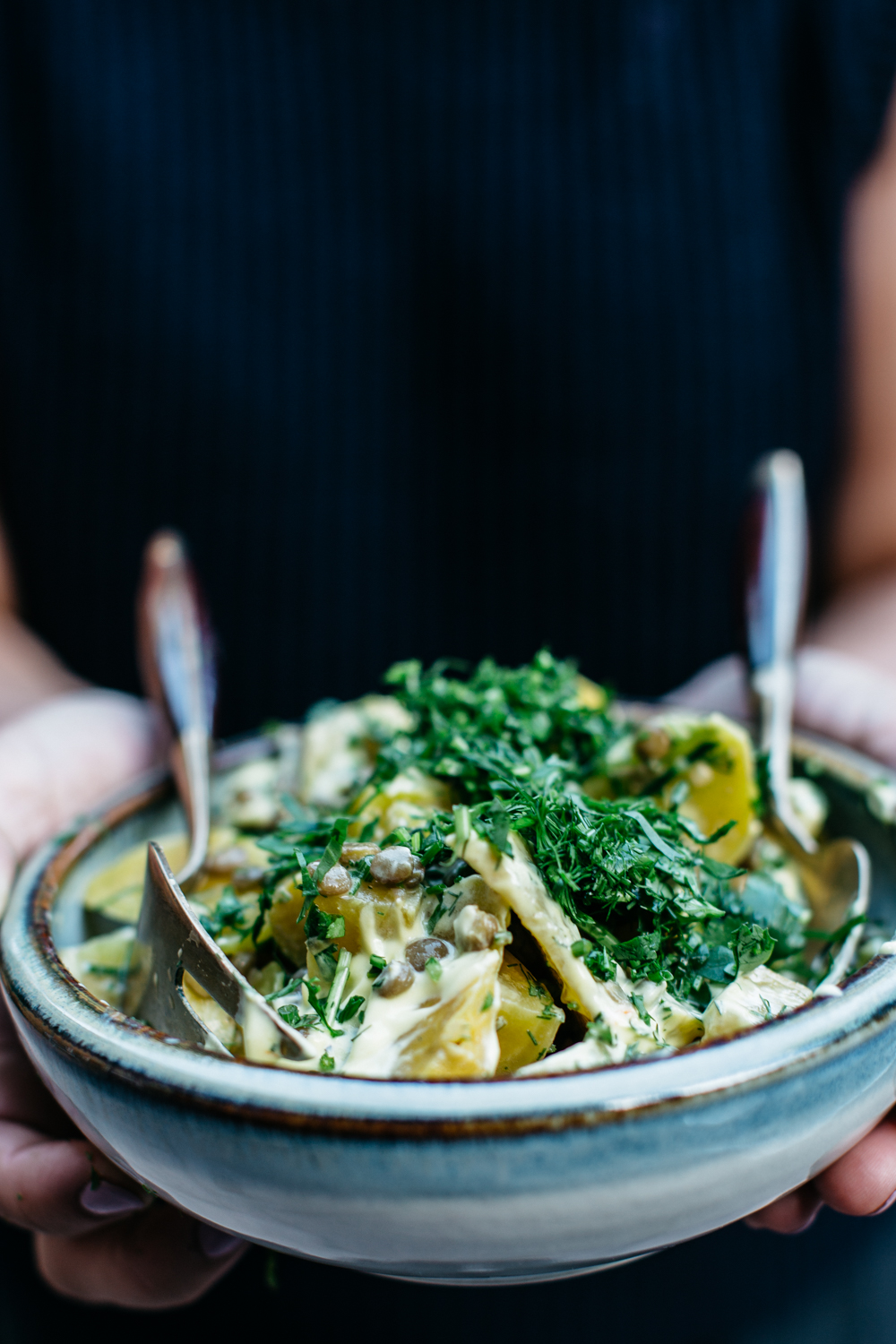 Bowl of potato salad with creamy dressing and fresh herbs, held by a person.
