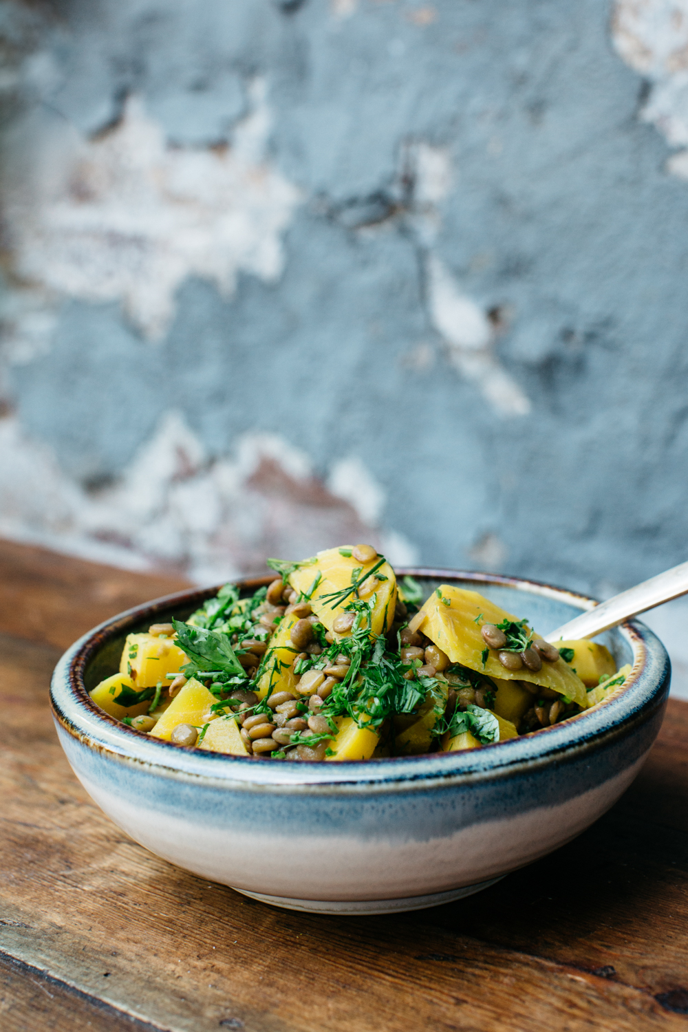 Bowl of potato salad with herbs and lentils on wooden table.