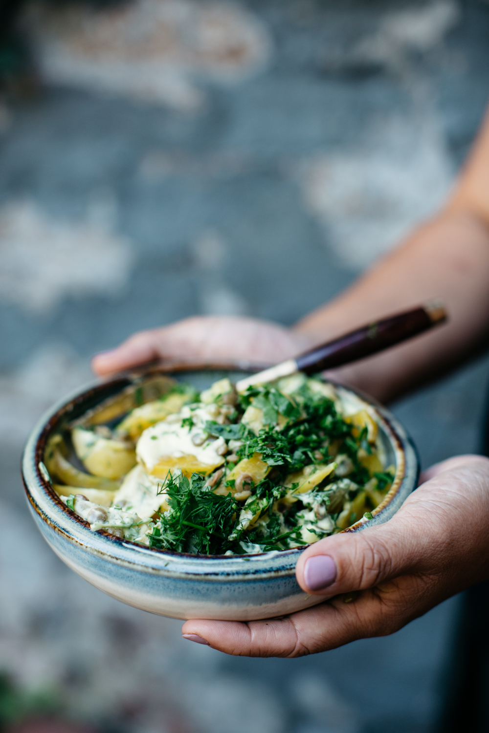 Hand holding a bowl of pasta with creamy herb sauce and fresh greens.