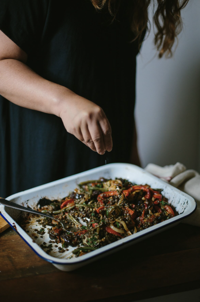 Person seasoning a tray of roasted vegetables with herbs.