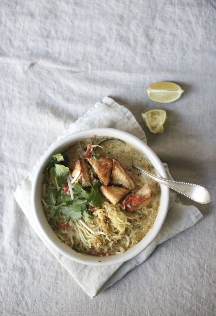 Bowl of noodle soup with tofu, cilantro, and lime on a cloth surface.