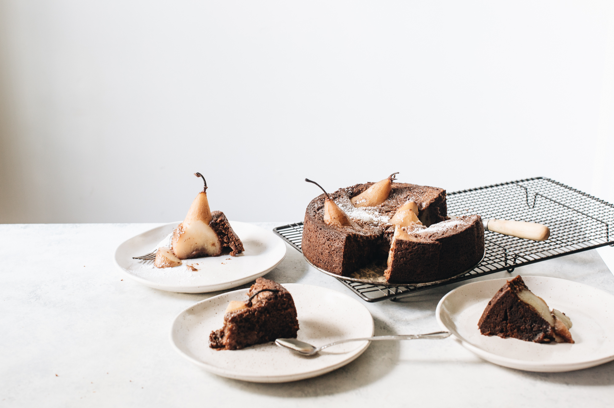 Chocolate cake with poached pears, served on a cooling rack and on plates with forks and a spoon.